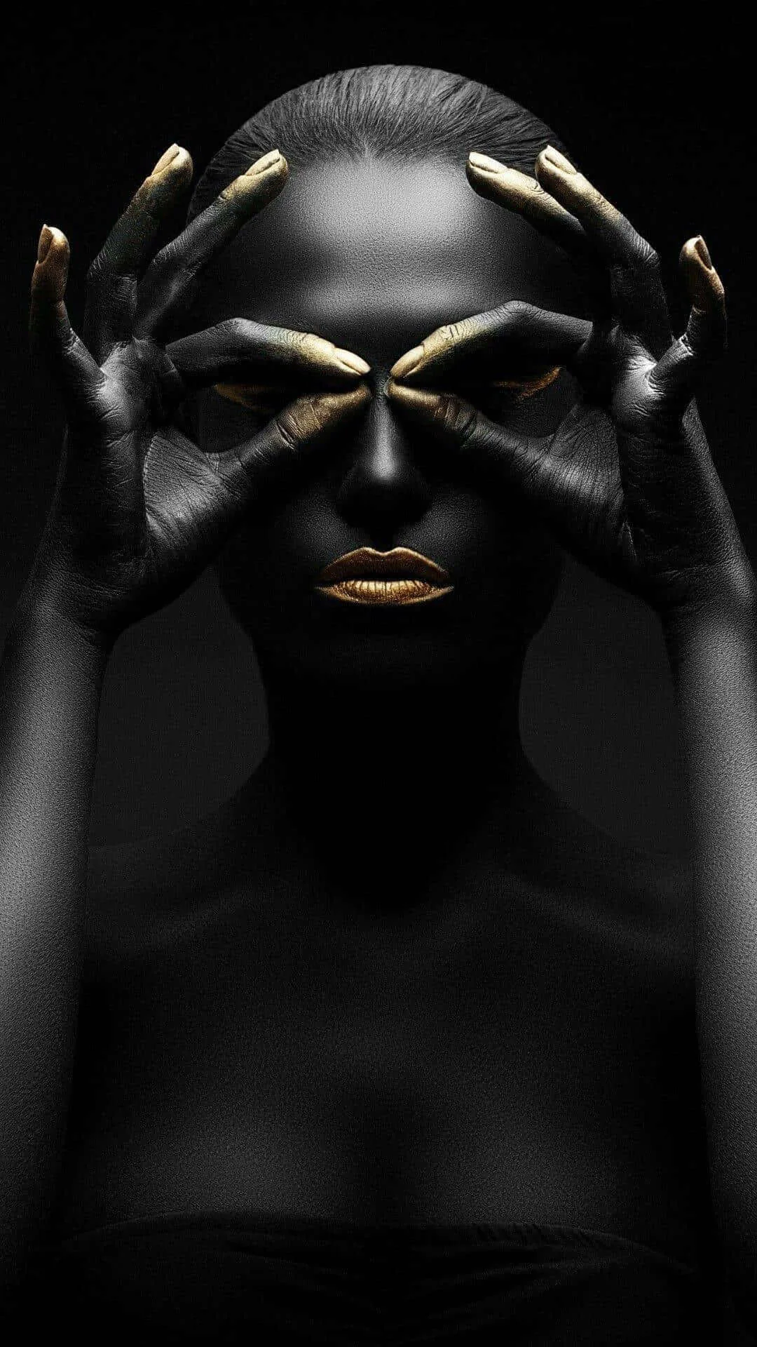 A woman painted head to toe in matte black holds finger circles around her eyes, gold lips and nails the only colour, the lower third staying dark for icons.