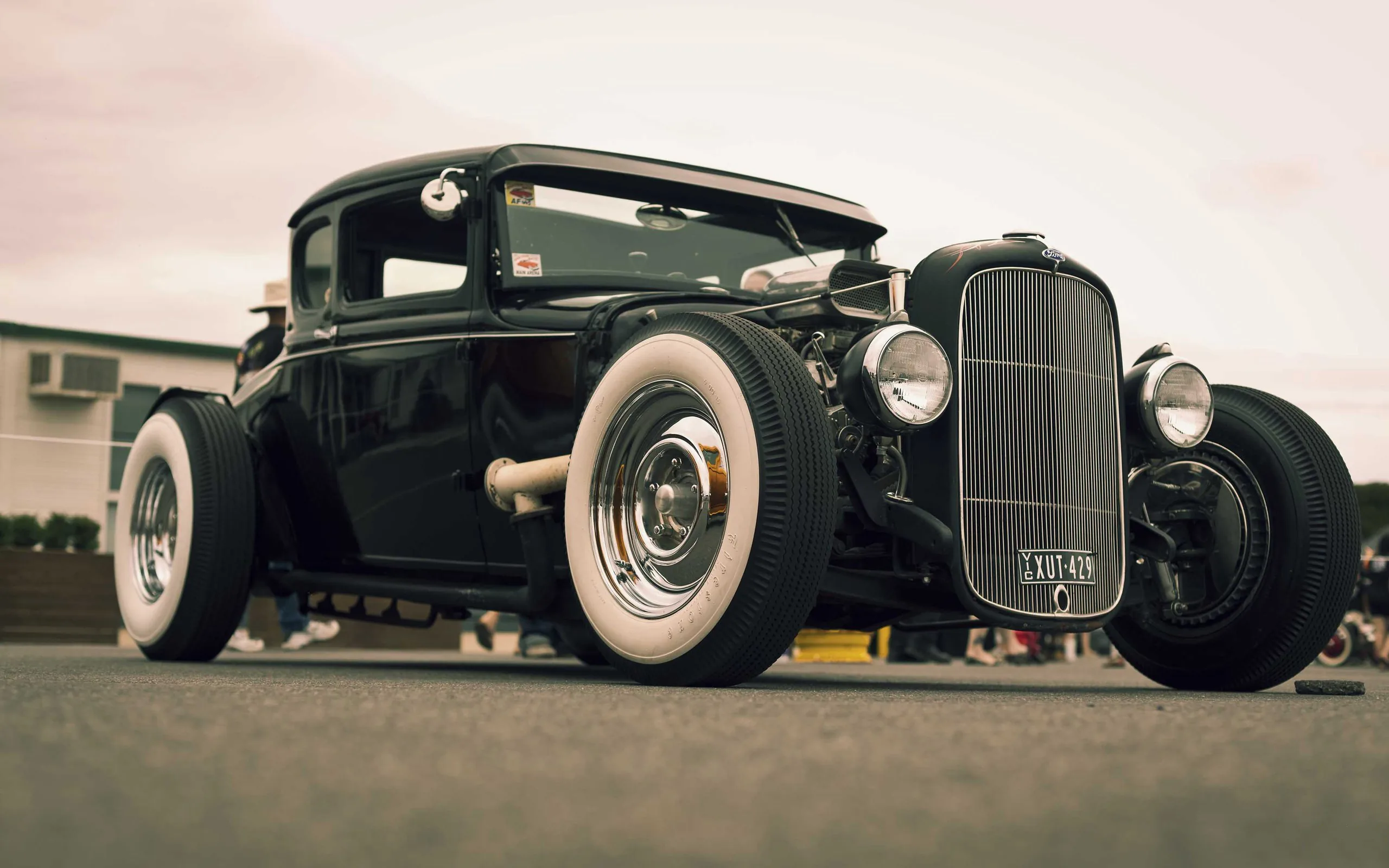 A chopped hot rod coupe on wide whitewall tyres looms over the camera, its chrome grille catching light under a faded pink evening sky left clear for icons.