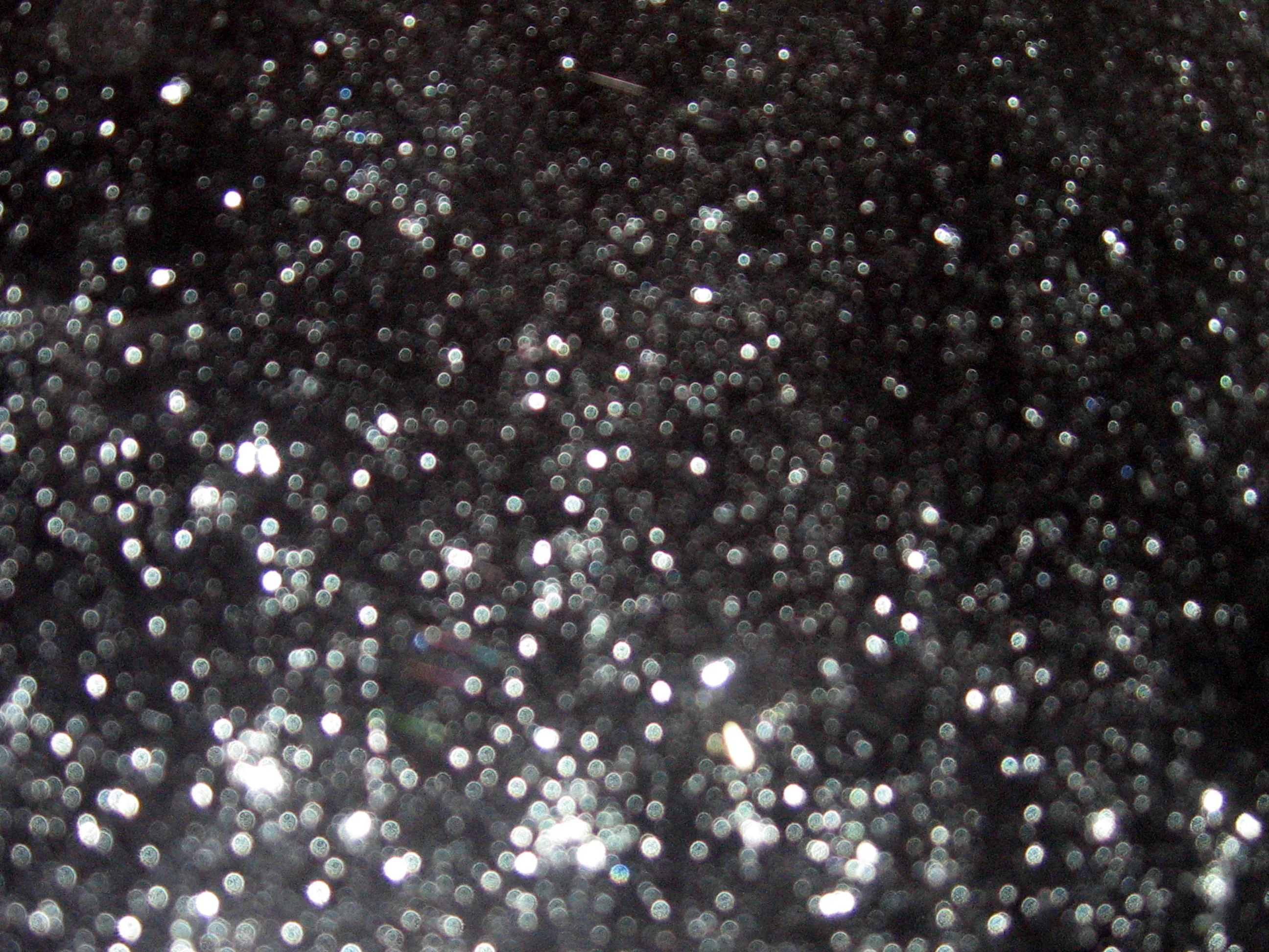 Defocused silver glitter with soft round highlights growing larger toward the lower-left, the top edge staying in dim shadow above the sparkle.