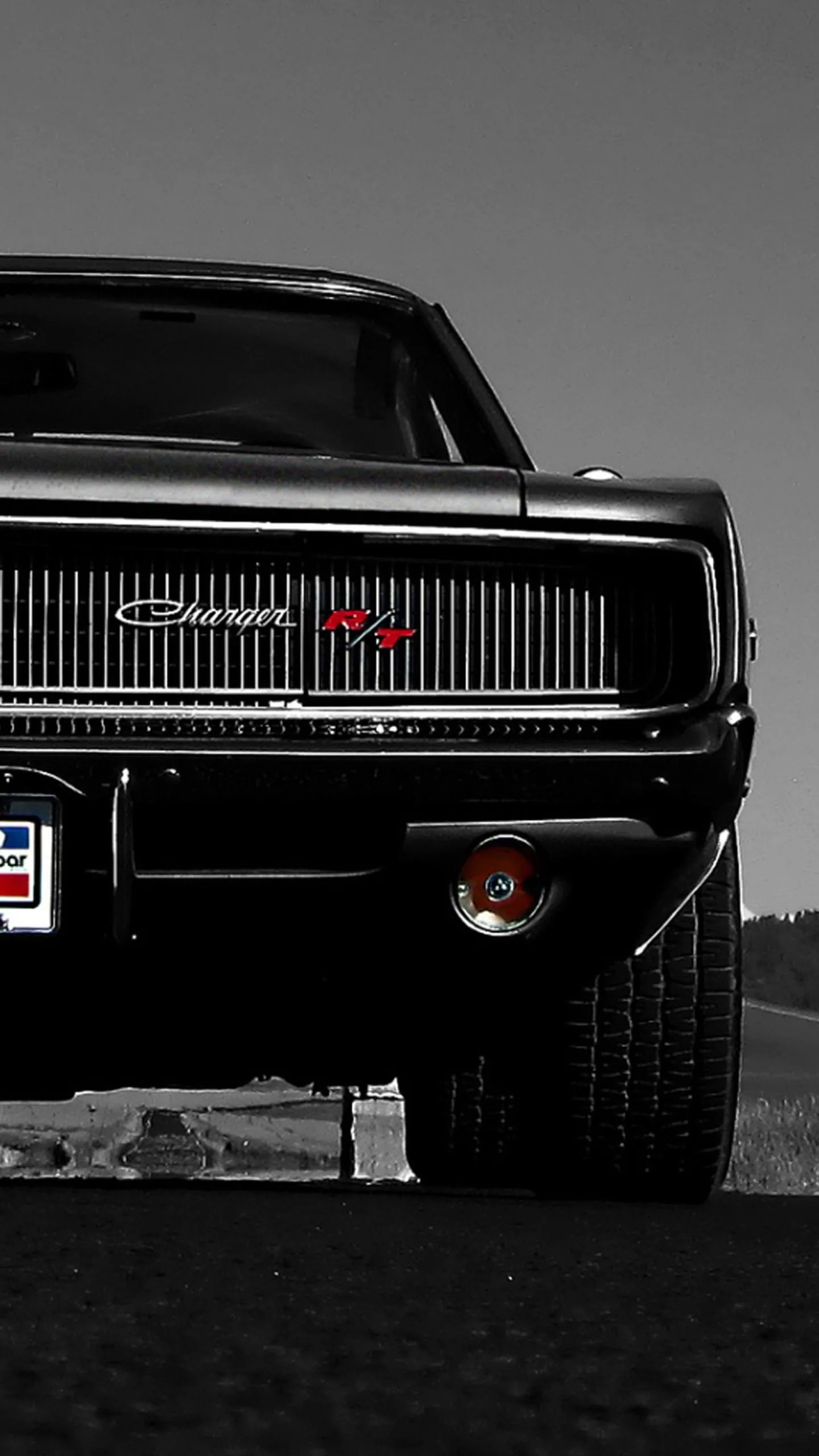 The blacked-out grille and hidden headlamps of a classic muscle car fill the lower half of the frame, chrome badges and a round rear lamp catching what light there is.
