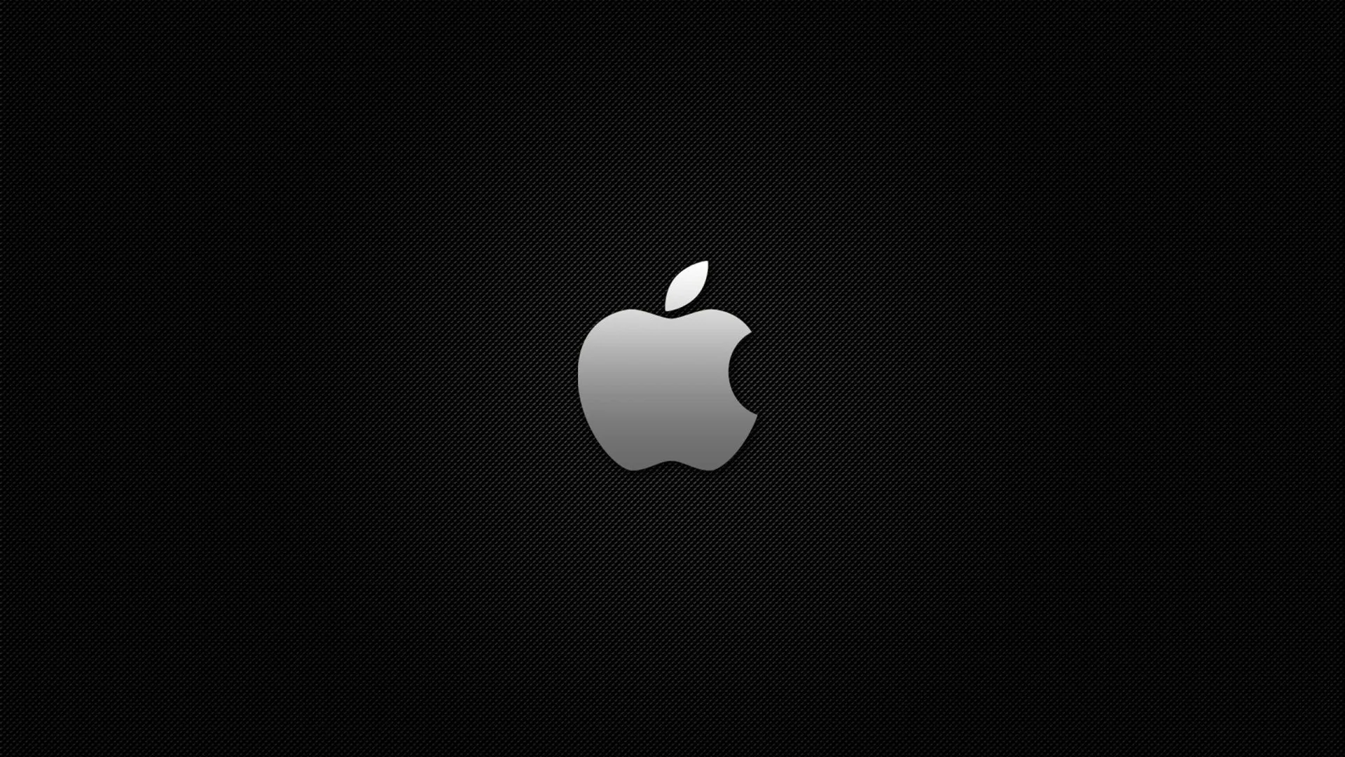 A silver Apple mark sits in the middle of a wide black frame, a soft halo of grey light spreading out behind it and fading at the corners.