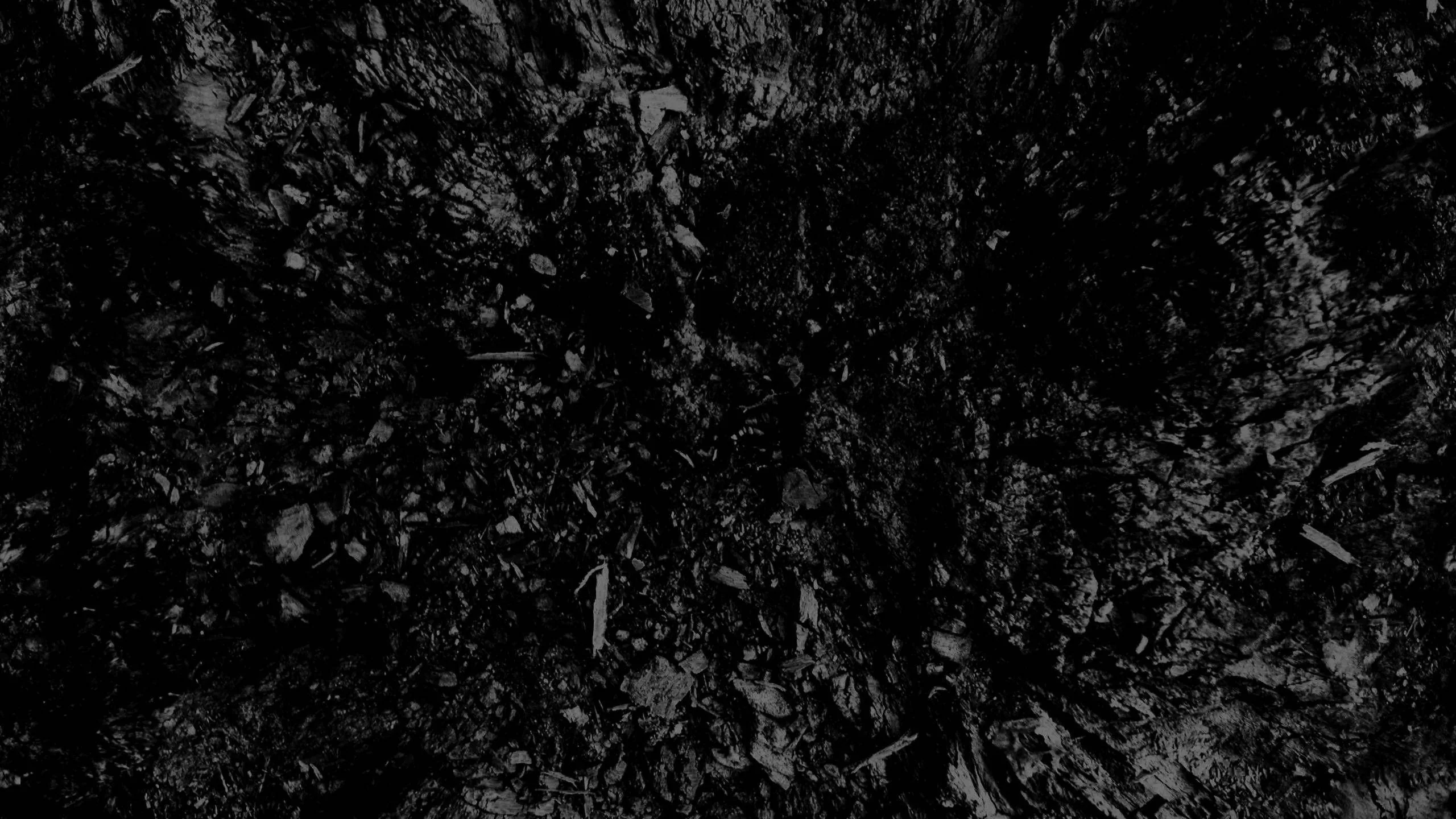 Broken flakes of charcoal scattered over a black ground, the light dropping off hard toward every corner of the wide frame.