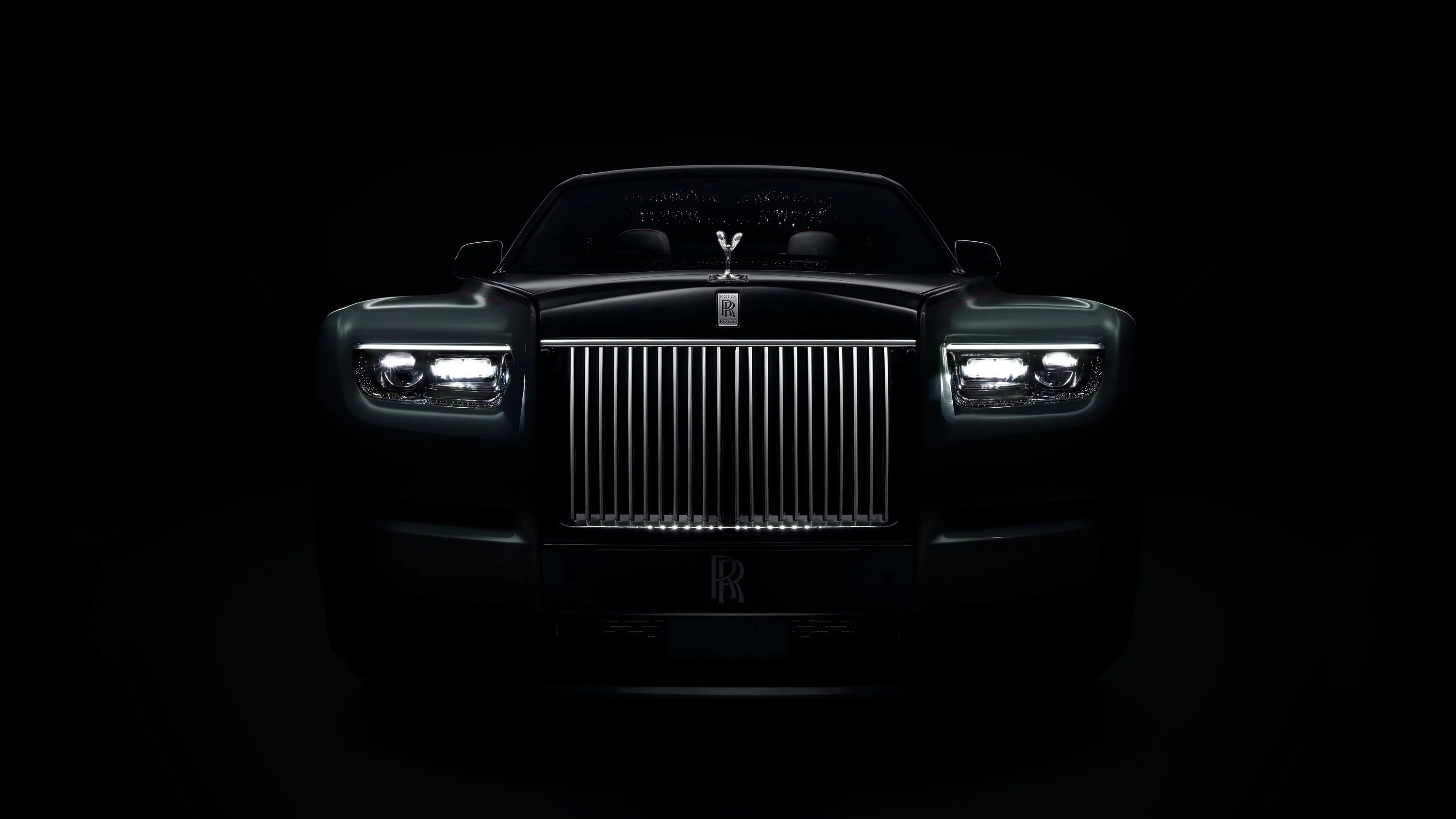 The saloon faces the camera on a black background, chrome vanes of the grille and the two slim LED headlamps carrying almost all of the light in the frame.