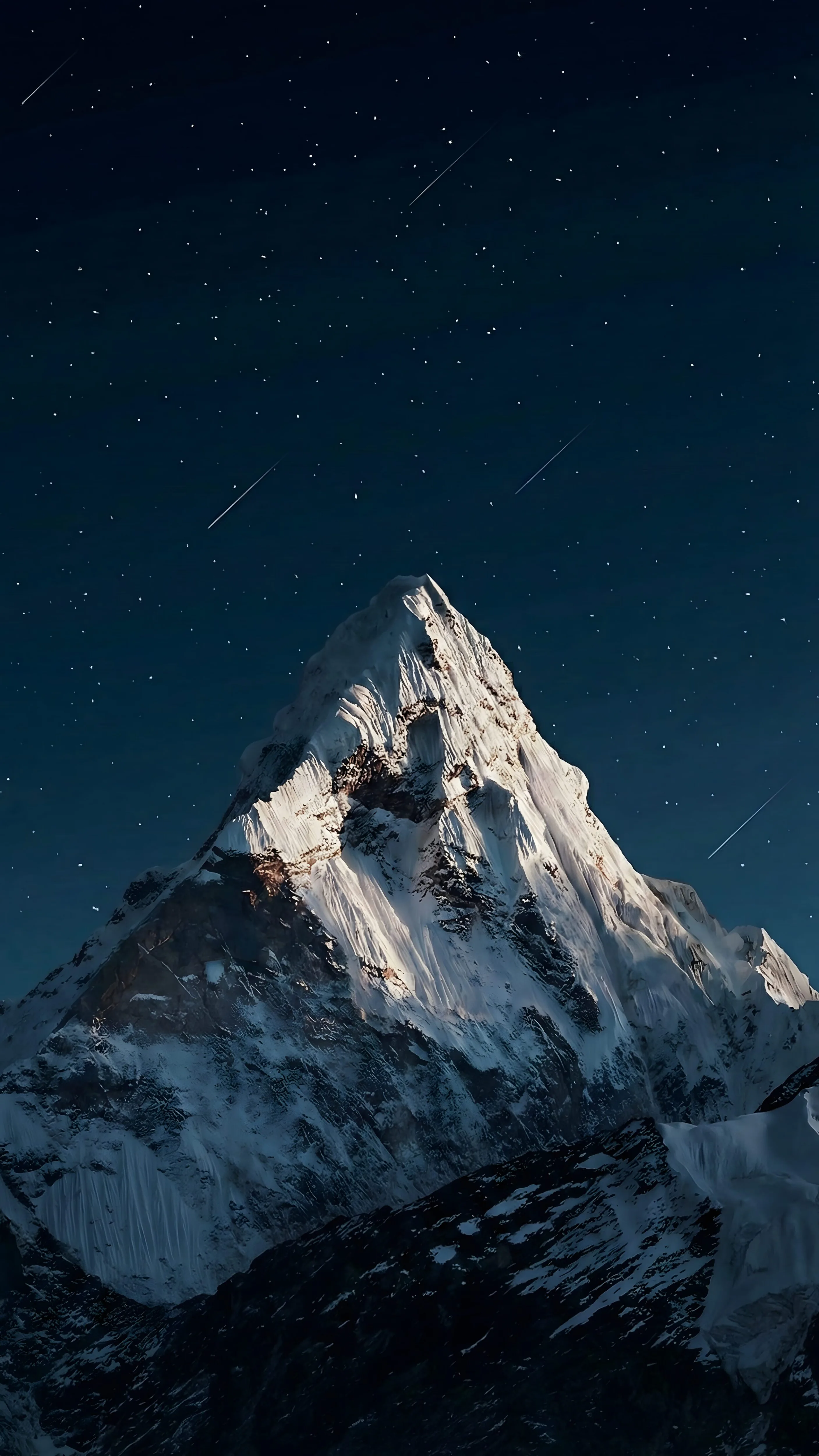 A sharp snow-covered peak rises into a star-filled night sky, moonlight catching the ridge on the left while the base stays in shadow.