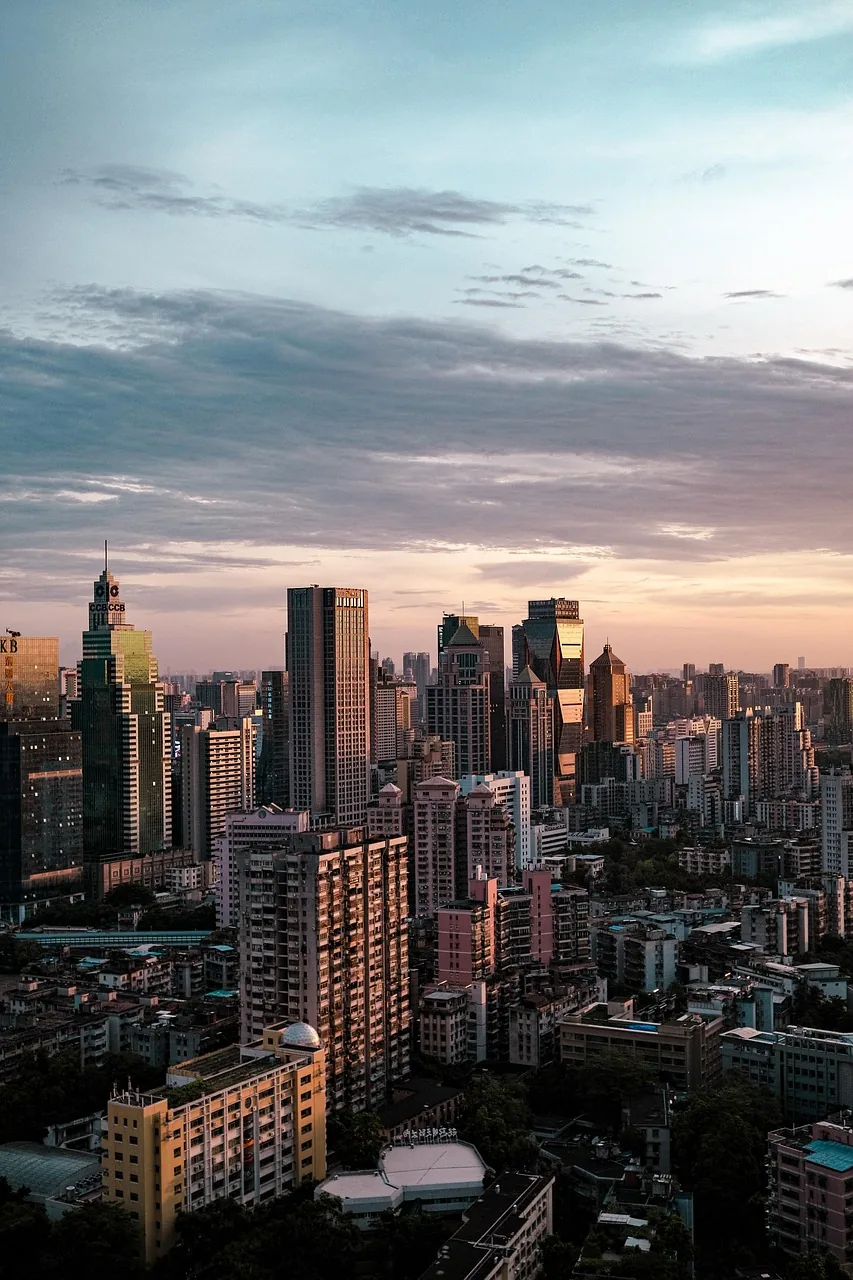 Downtown towers catch the last warm light of the day under a pale blue sky, dense rooftops filling the lower half of the frame.
