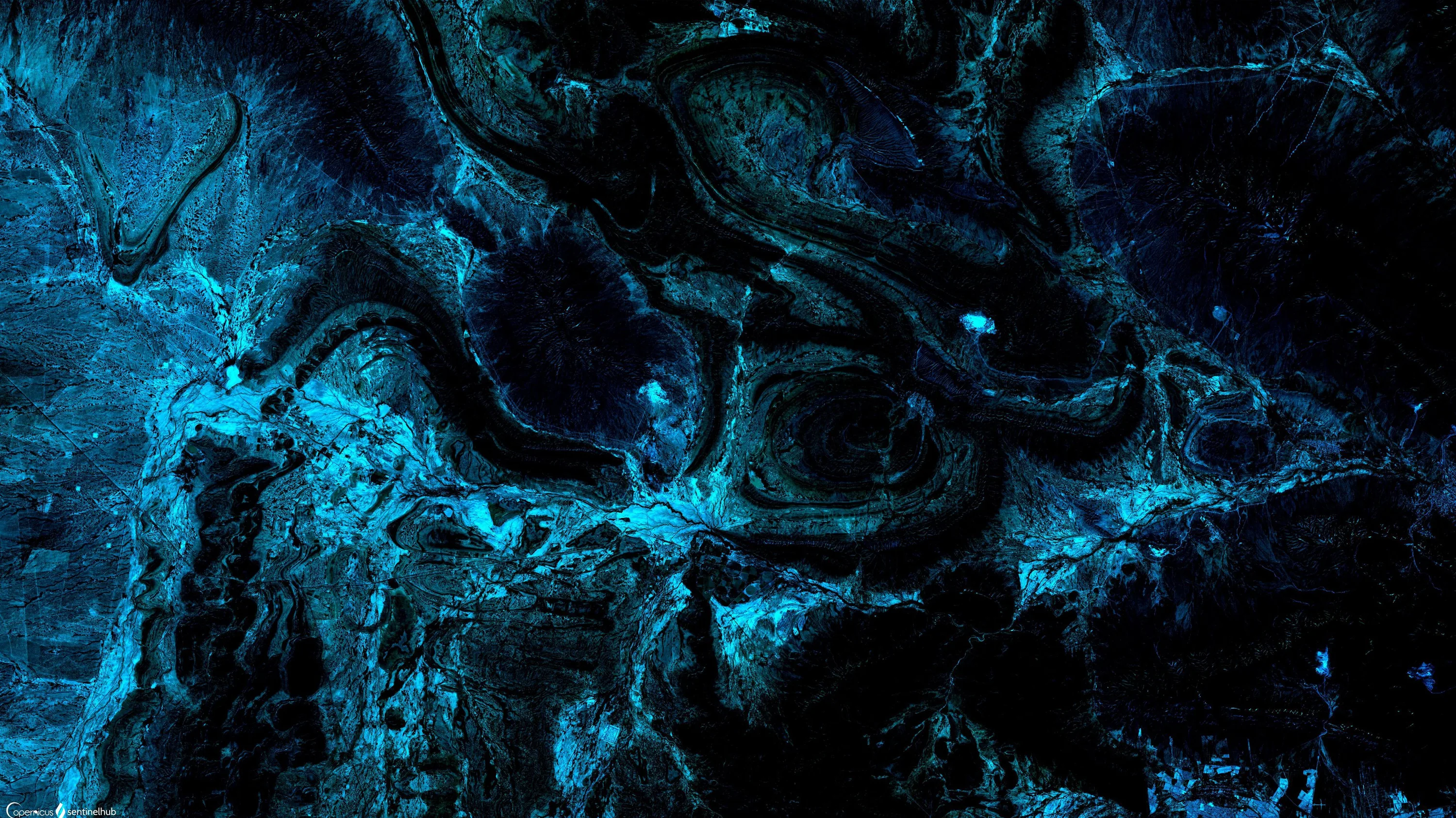 Wet rock ledges photographed from above, every ridge outlined in cold teal while the hollows stay black.