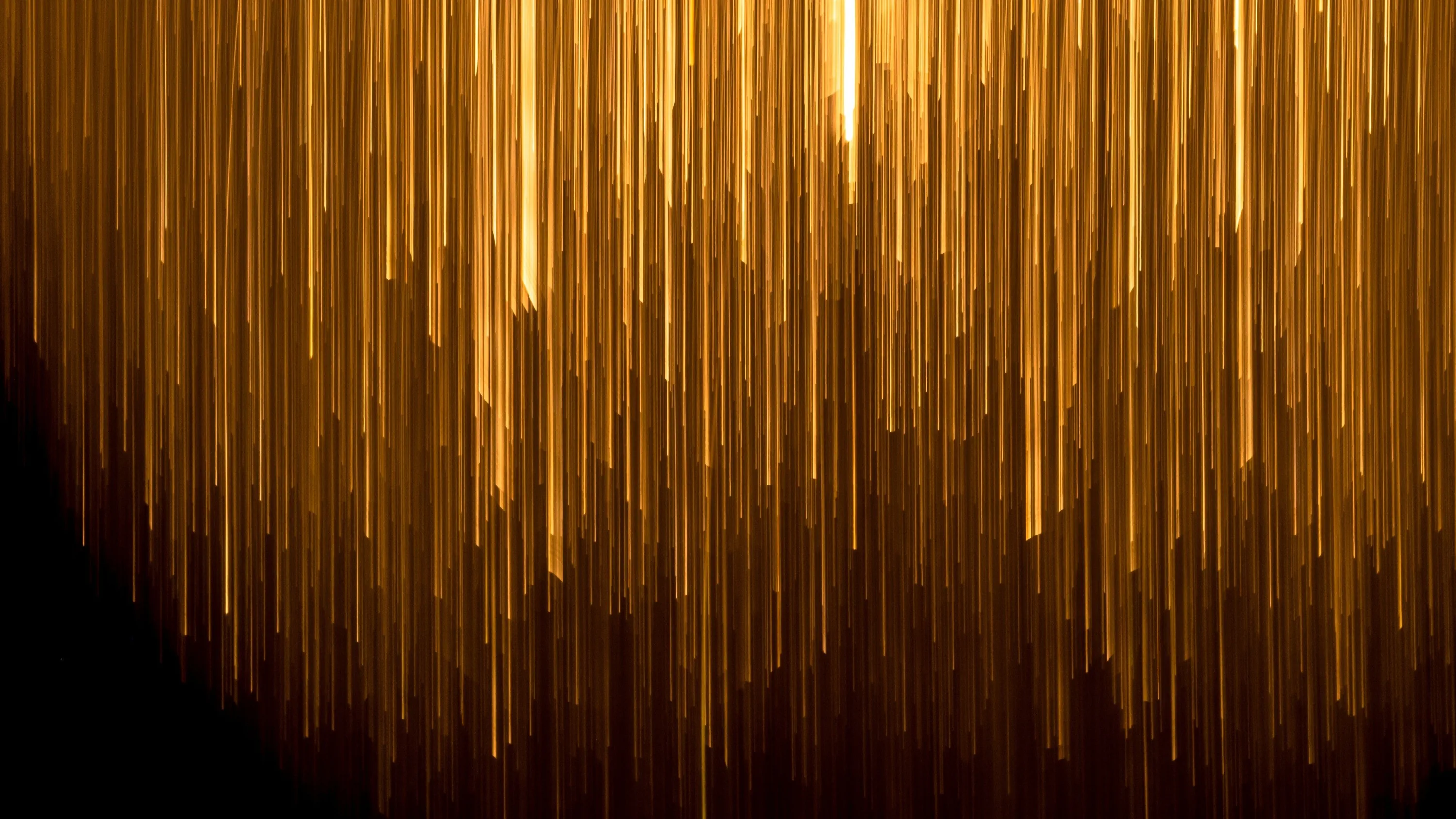 Vertical bars of amber light drop like rain, brightest at top centre, while the lower left corner sinks into solid black.