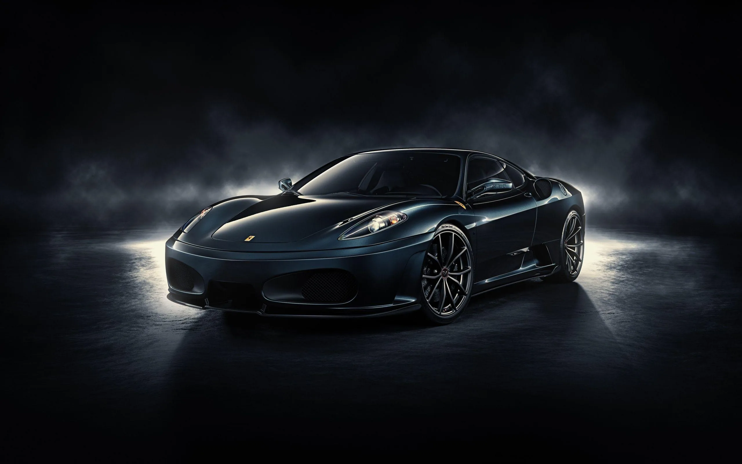Thin smoke drifts across a dark studio floor around a black F430, side lights raking the sills and leaving the roof and windscreen almost unlit.
