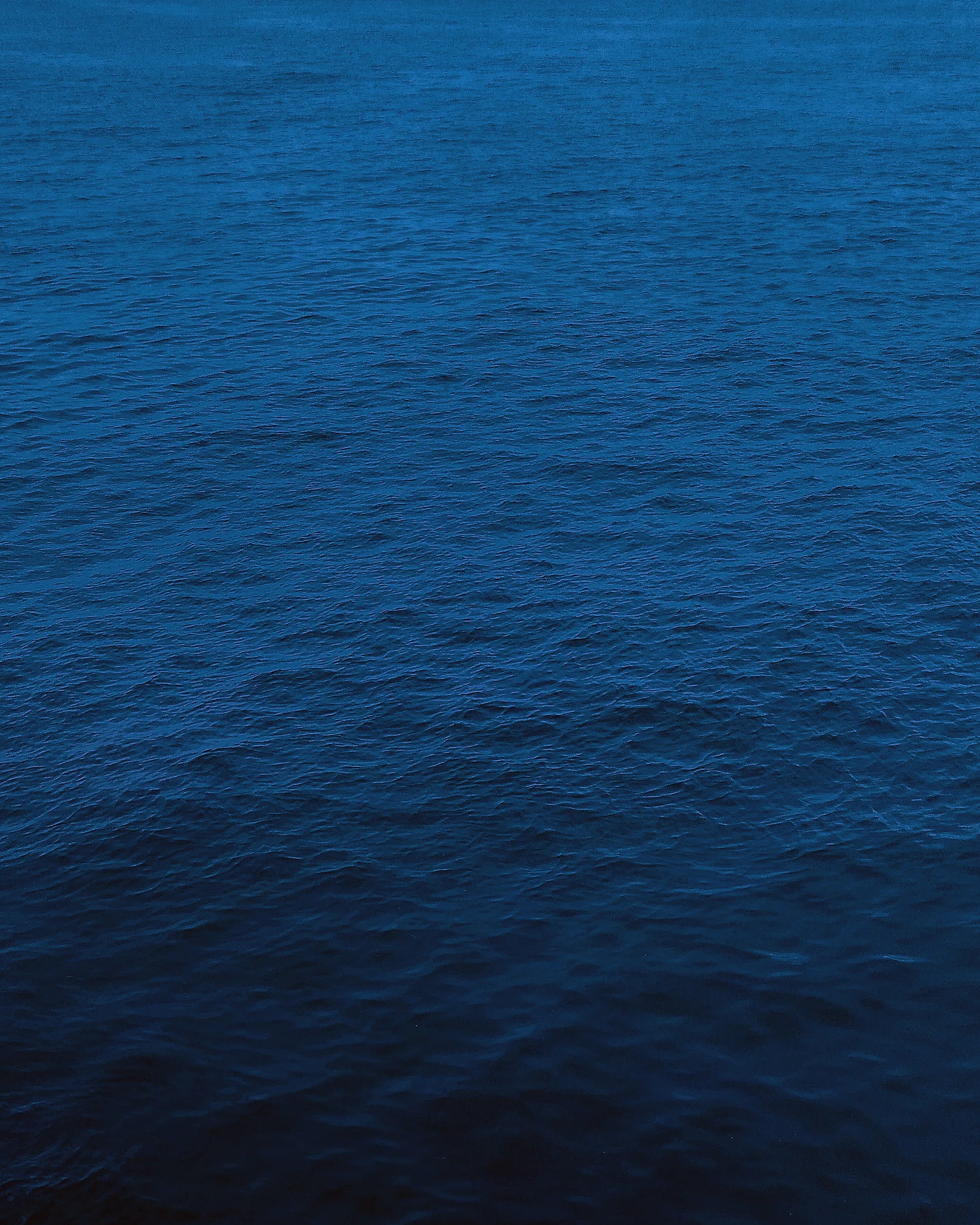 A calm sheet of navy sea fills the tall frame with barely a ripple, slightly lighter at the top and shading darker toward the bottom edge.
