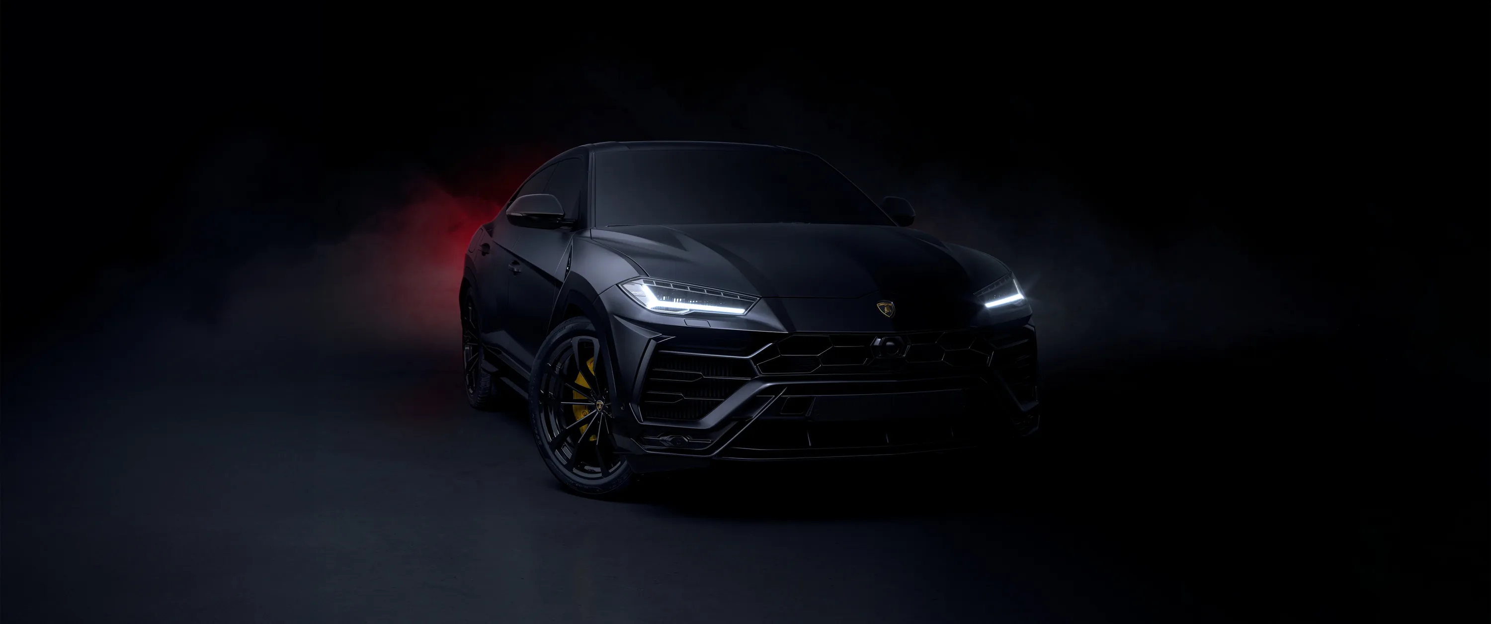 Only the SUV's headlamps and front edges catch light, the rest of the ultrawide frame sinking into near-total black for OLED screens.