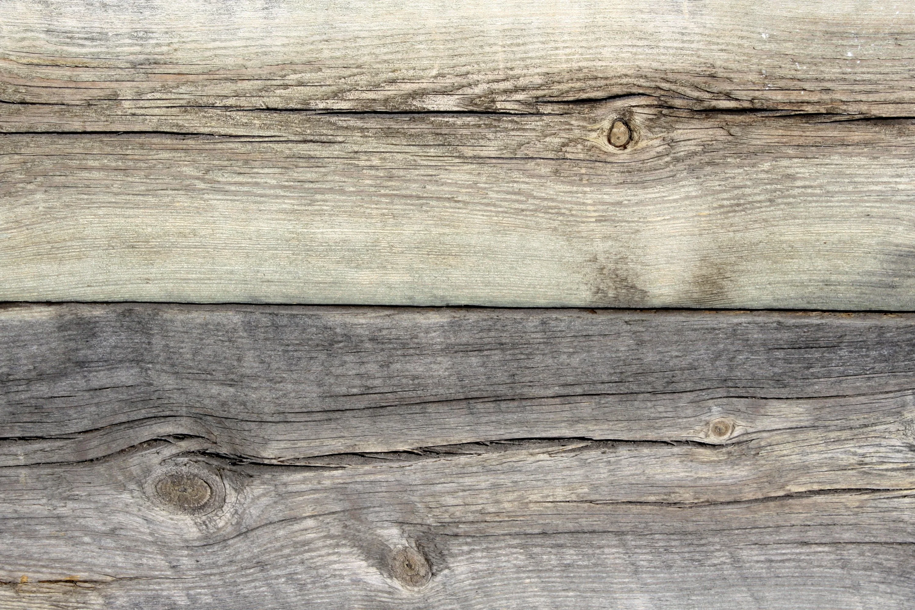 Sun-bleached planks run horizontally, the top half nearly white-grey and the bottom half a deeper grey, with a knot in the upper right and another lower left.