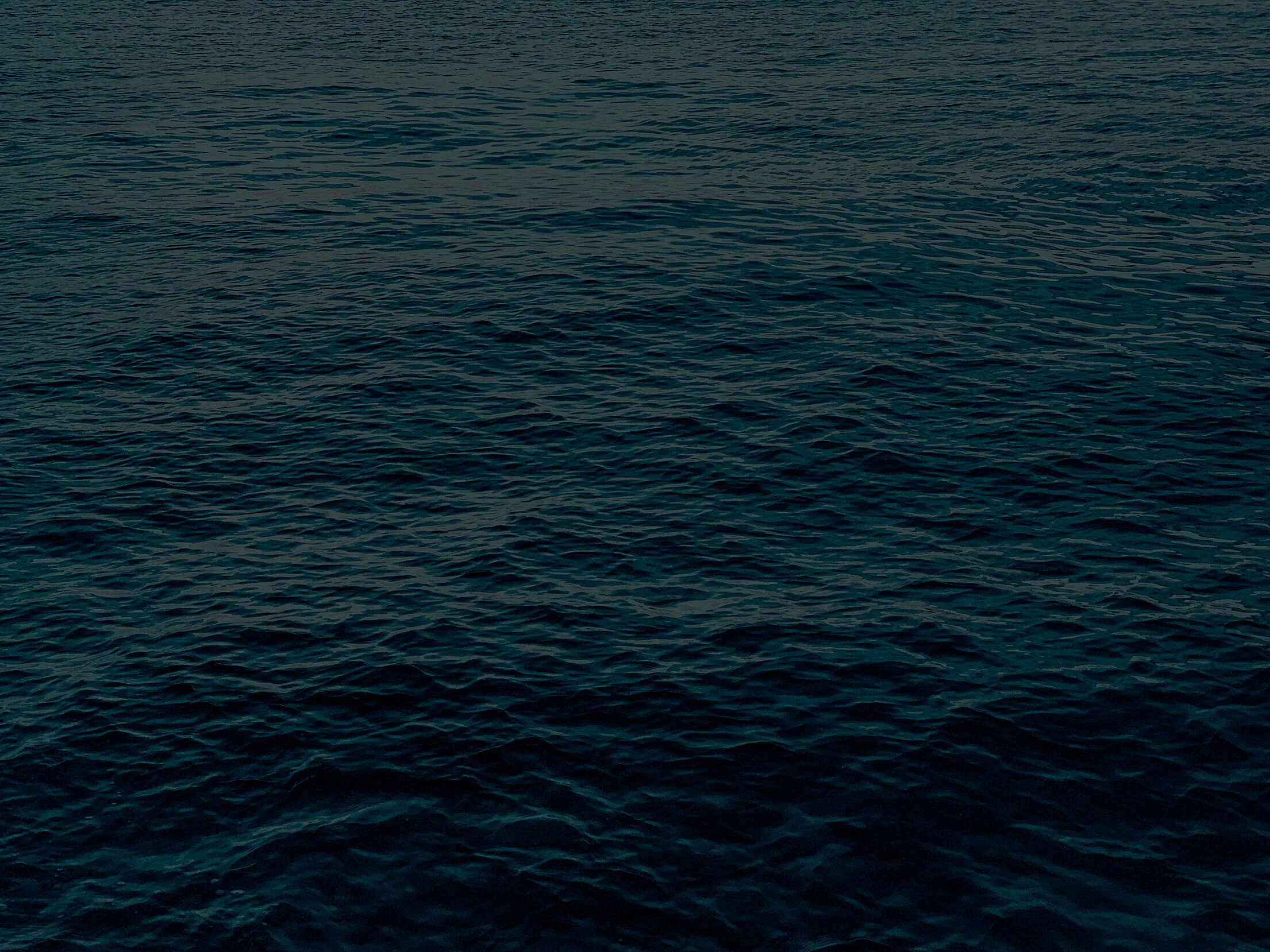 An expanse of sea at last light in a green-black teal, ripples fading with distance; dark enough overall that white widgets read anywhere.