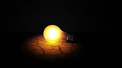 Lit Bulb Resting on Cracked Earth HD Wallpaper