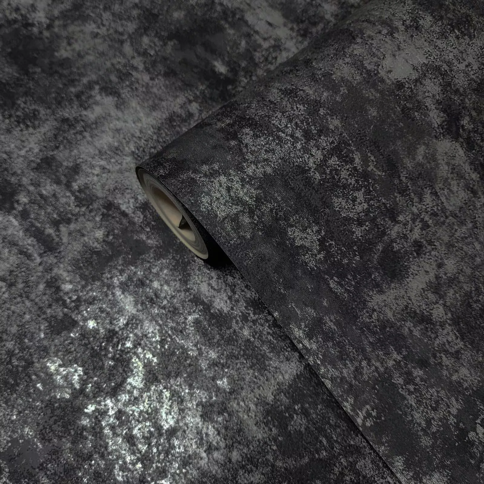 A rolled length lies diagonally across mottled charcoal plaster, a silvery sheen catching the lower left while the rest stays in matte greys.