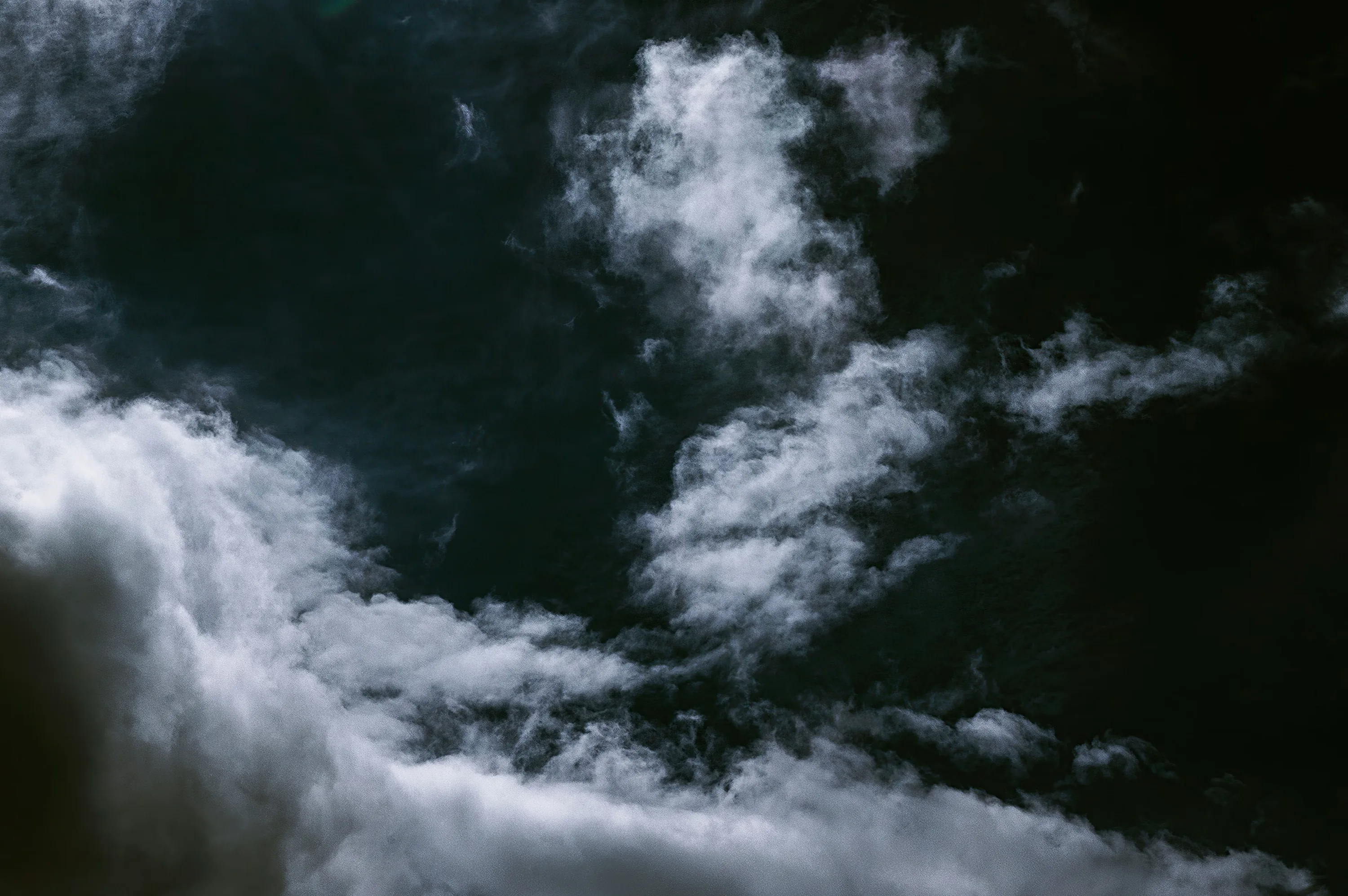 White clouds break up a near-black night sky, the brightest bank rising from the bottom left while the upper right stays dark.