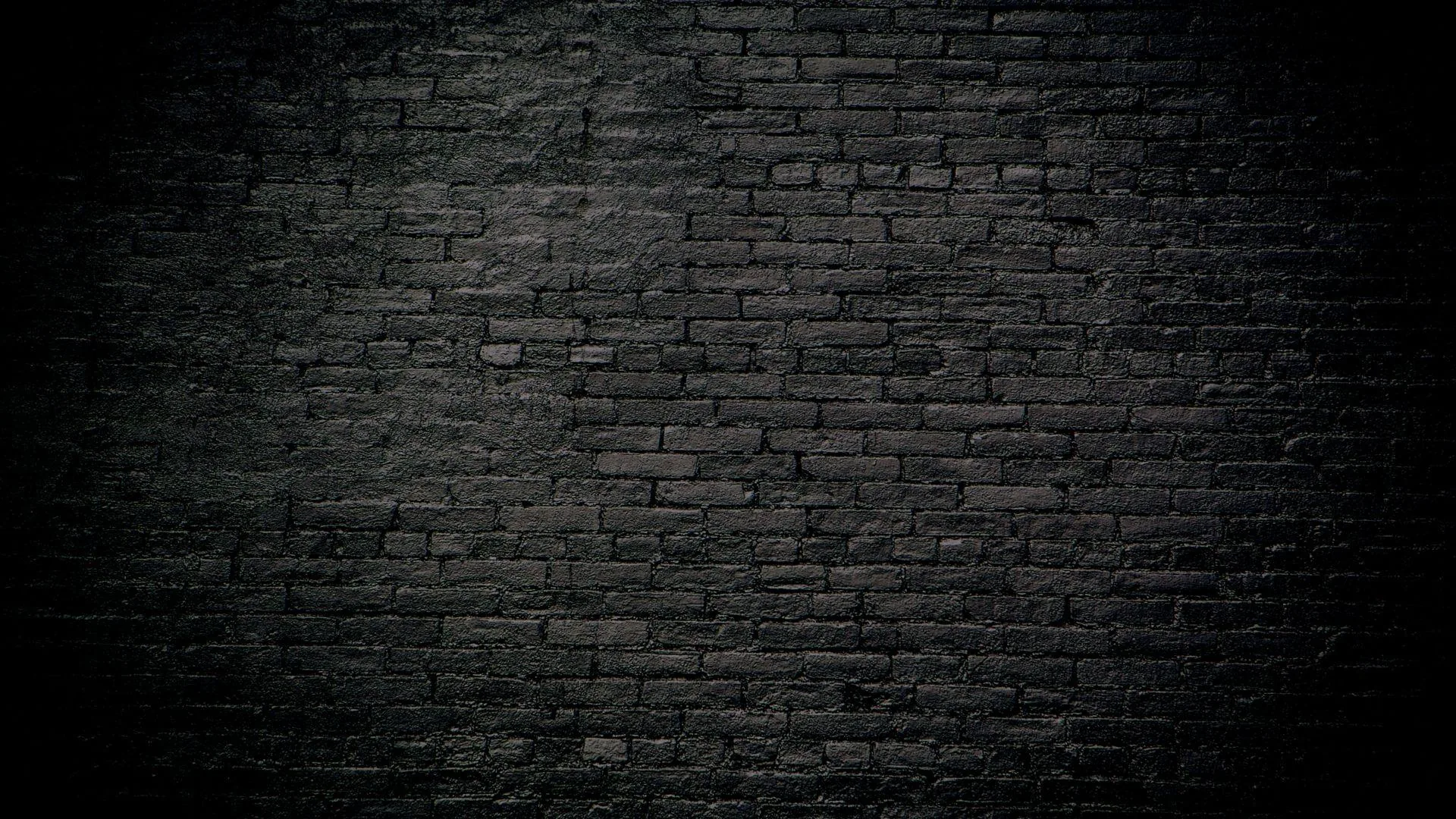 Painted black brickwork fills the frame, a soft glow across the middle rows fading to unlit corners on every side.