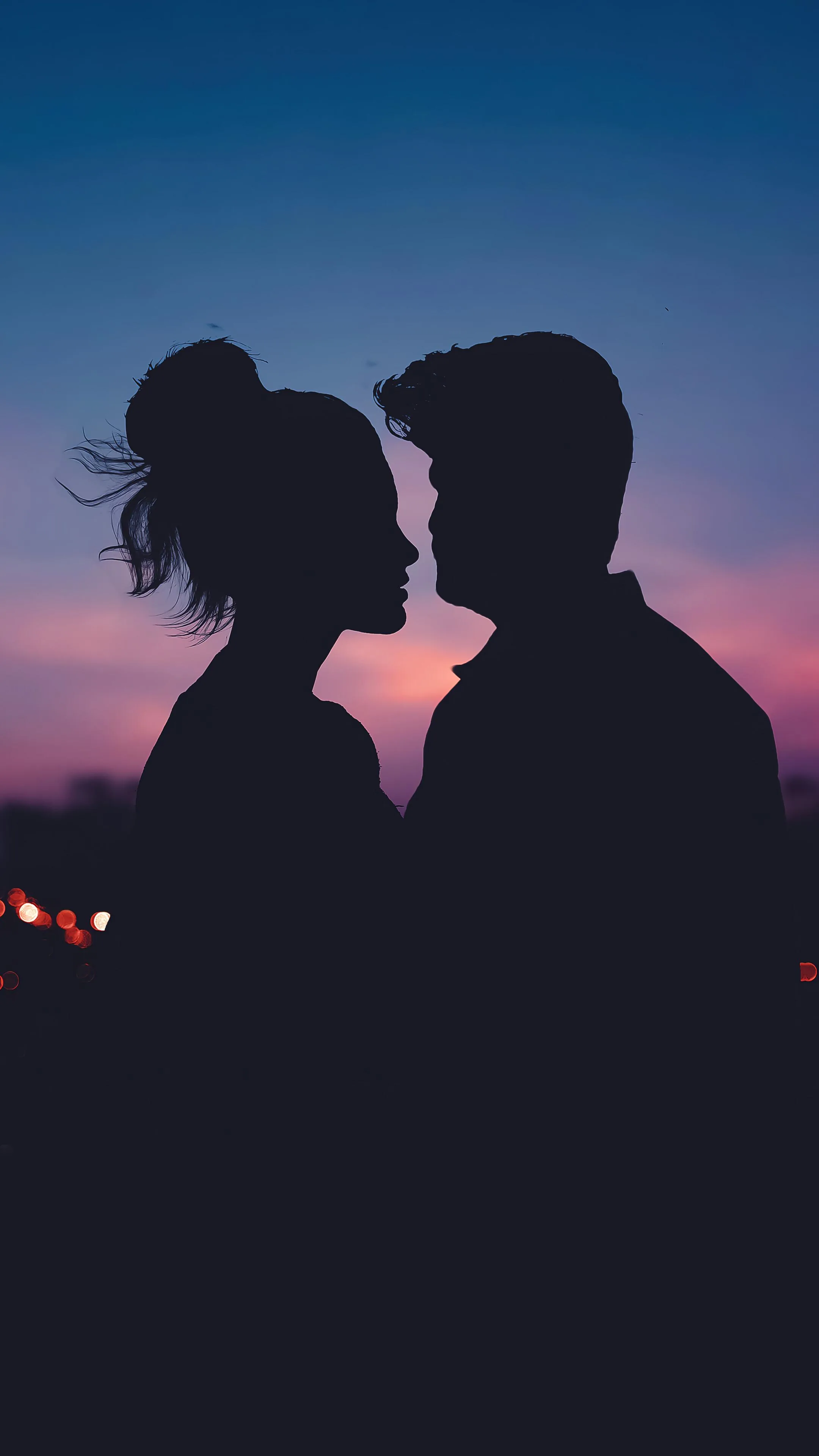 Two profiles hover a breath apart against a mauve and pink afterglow, blurred city lights dotting the lower edge while the upper half stays a smooth gradient.