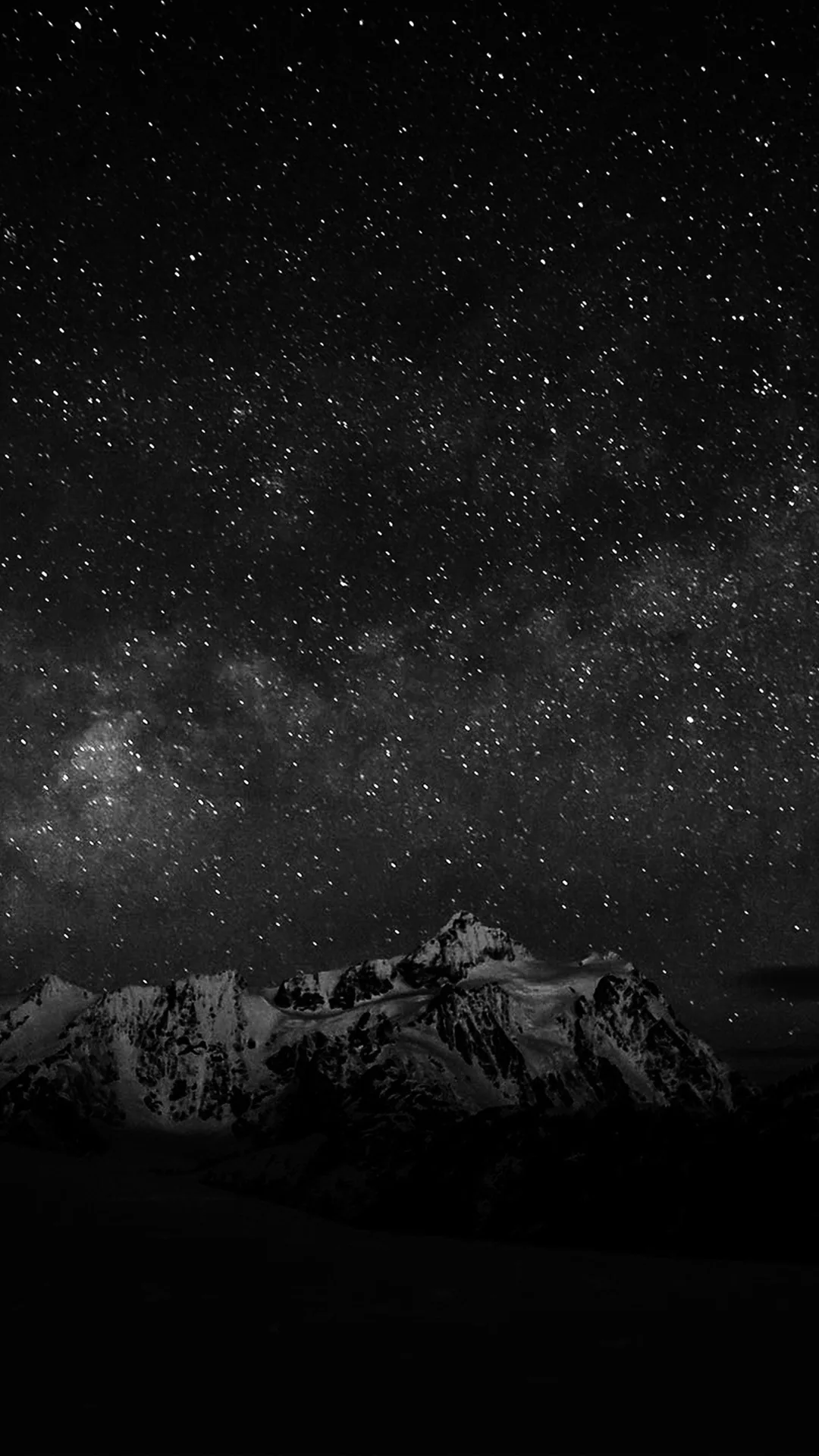 Black and white: a dense starfield and the Milky Way stretch above a jagged snow-capped ridge.