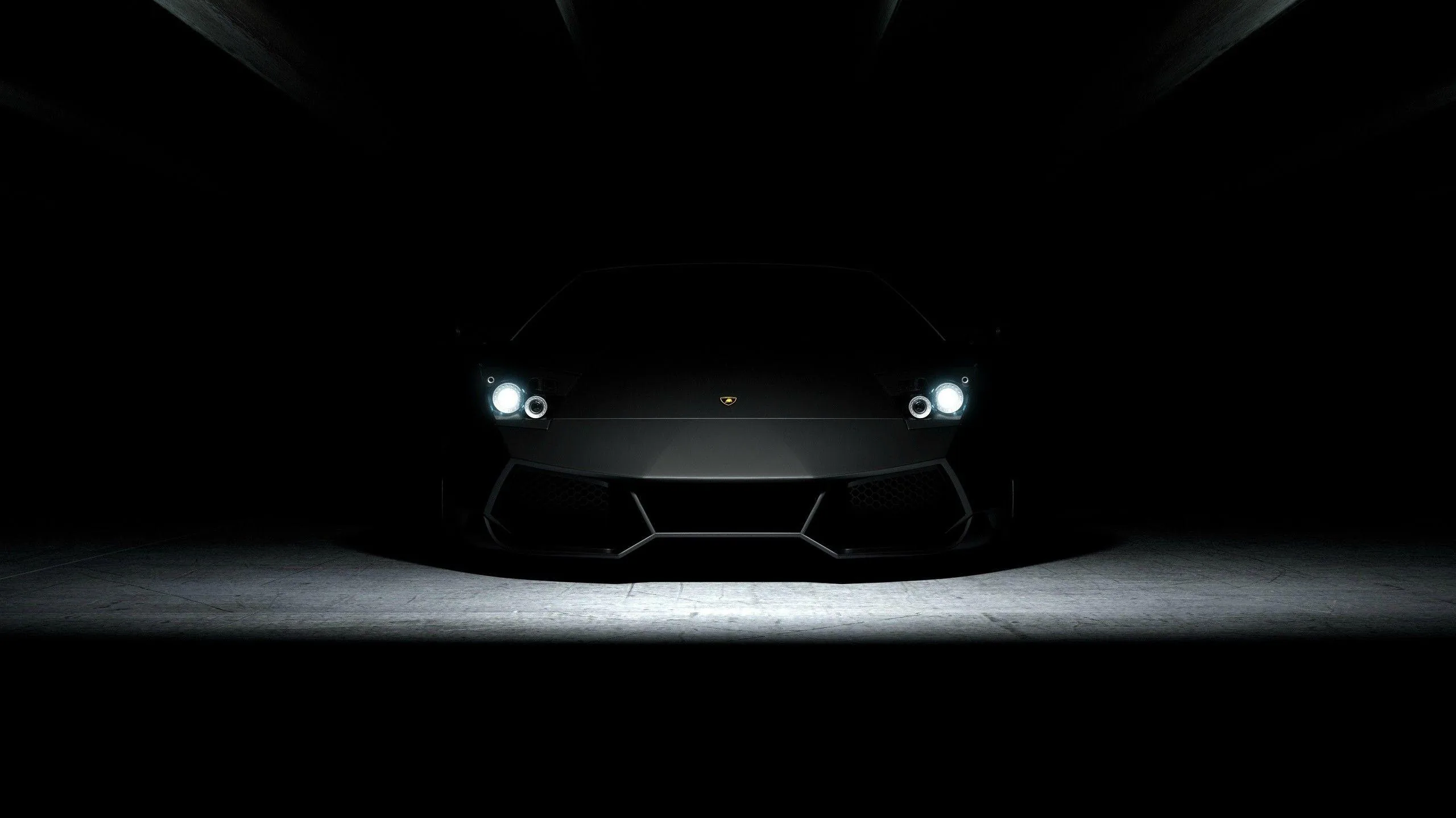 The car is almost fully swallowed by black, its shape read only from four white headlight points and the pale pool of light on the floor.