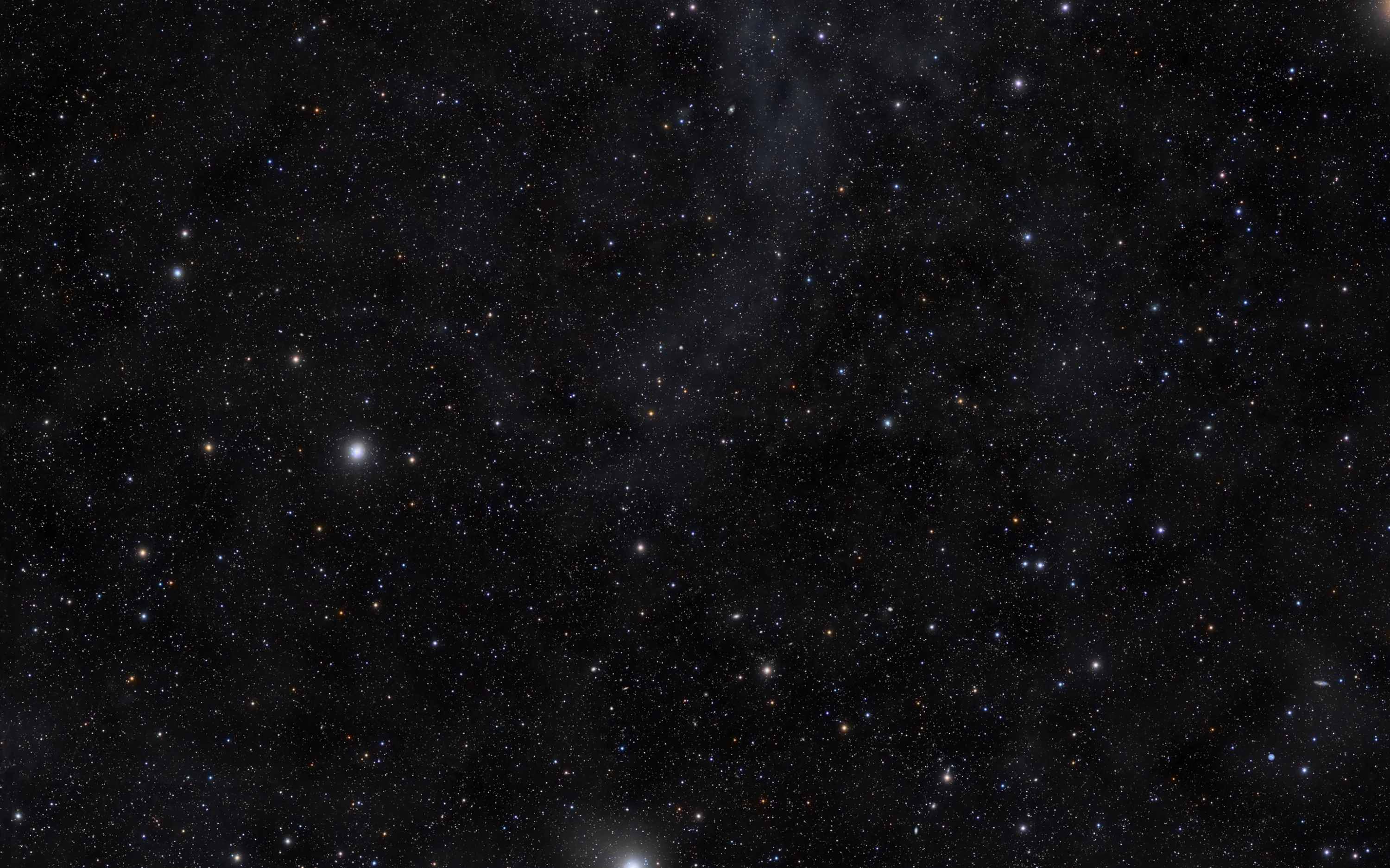 Thousands of small stars scatter across dark space with a faint dust cloud drifting through one corner.