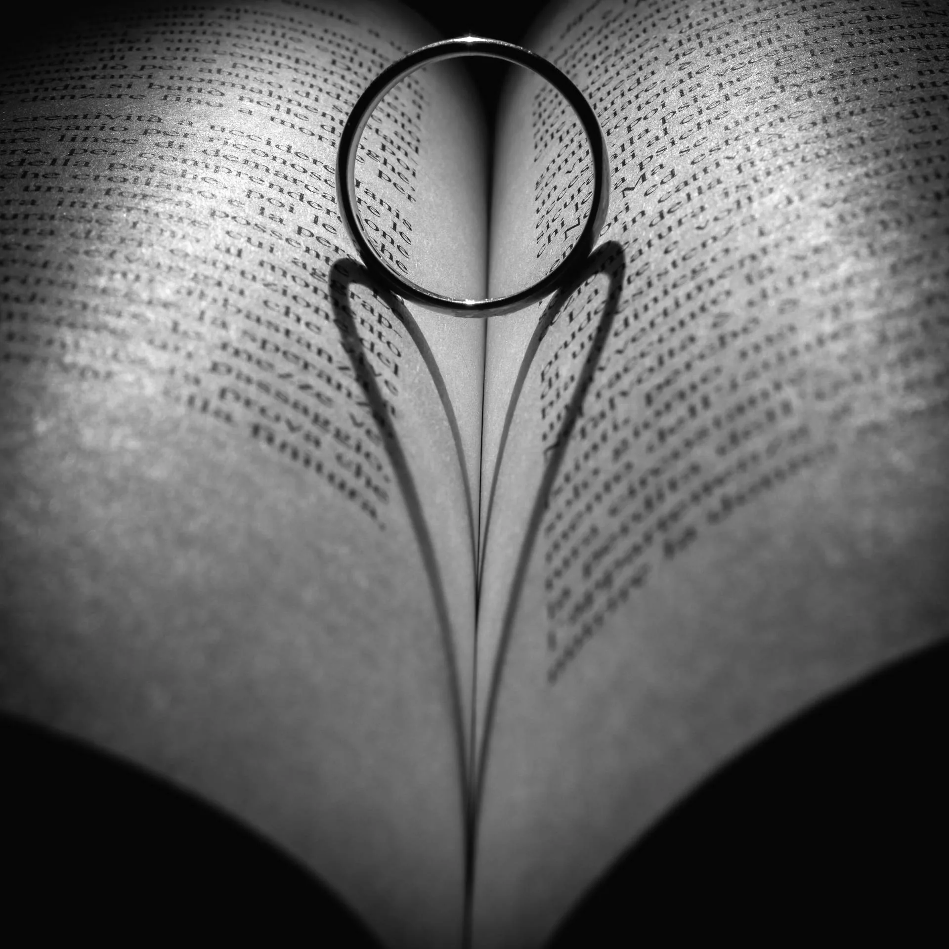 A plain band stands upright in the gutter of an open book and throws a heart-shaped shadow down both pages, the print blurring into grey toward the edges.