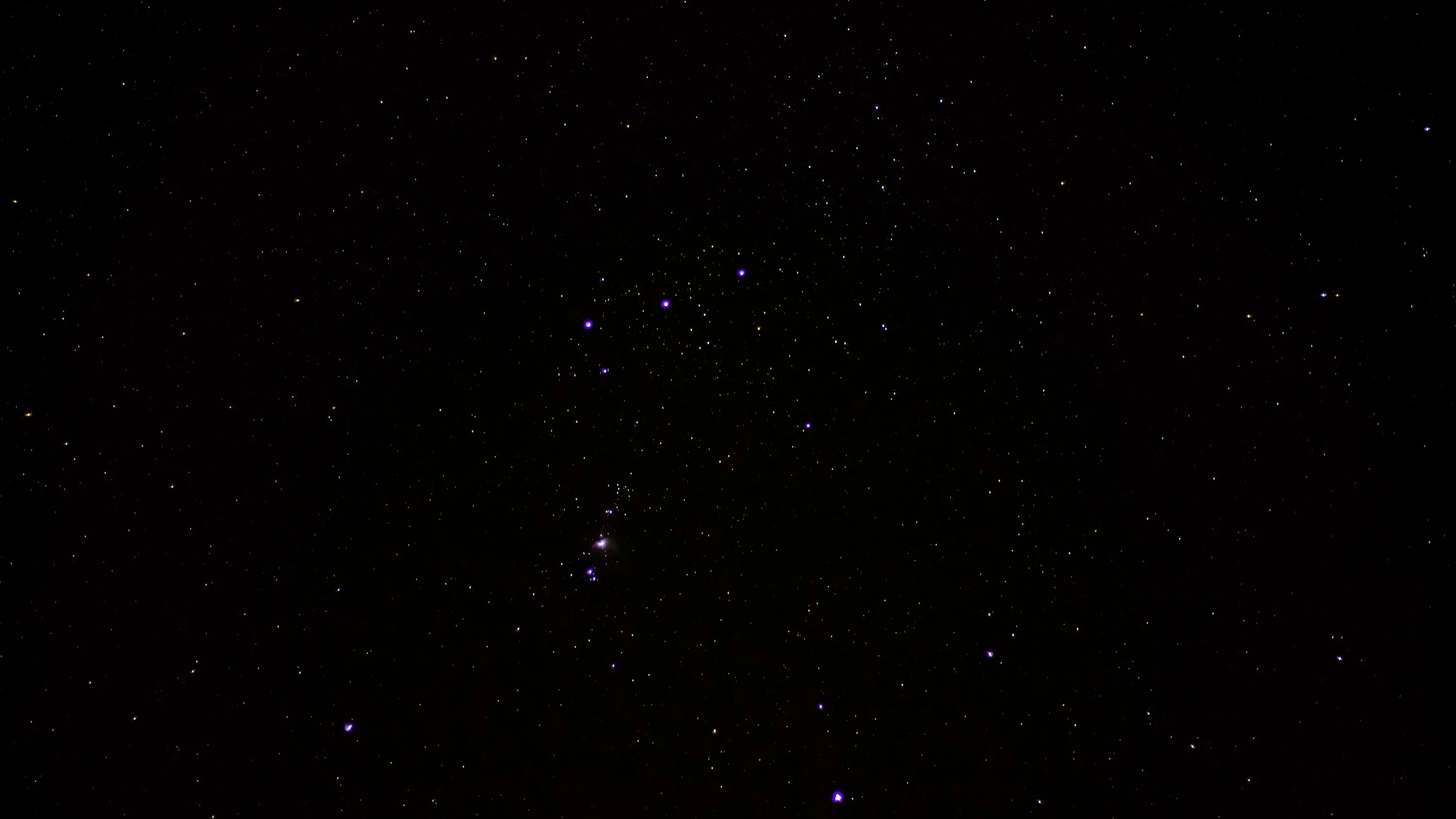 A photographic night sky that reads almost pure black, small blue and red stars grouped loosely near the centre, an easy background for OLED screens.