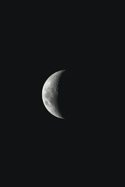 A waning crescent hangs in an otherwise empty black sky, craters visible along the lit edge.