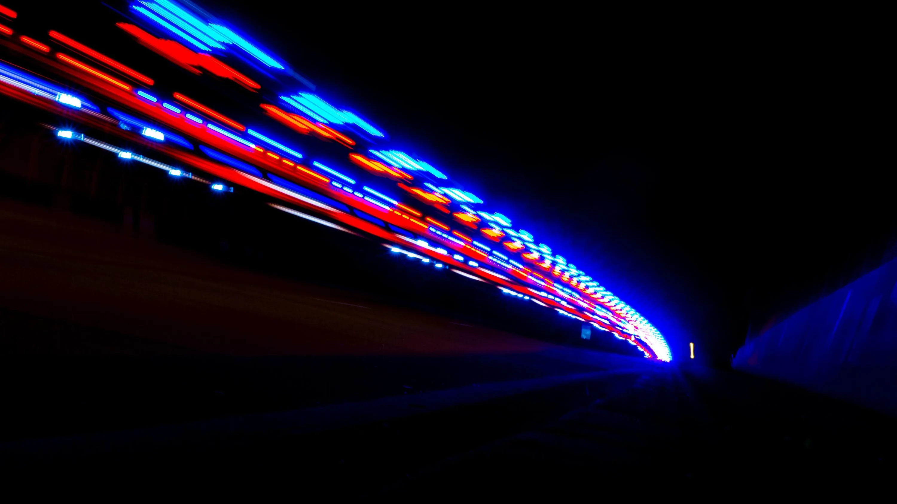 Red and blue light trails streak from the left toward a vanishing point inside a dark tunnel, the right half of the frame dropping to black.