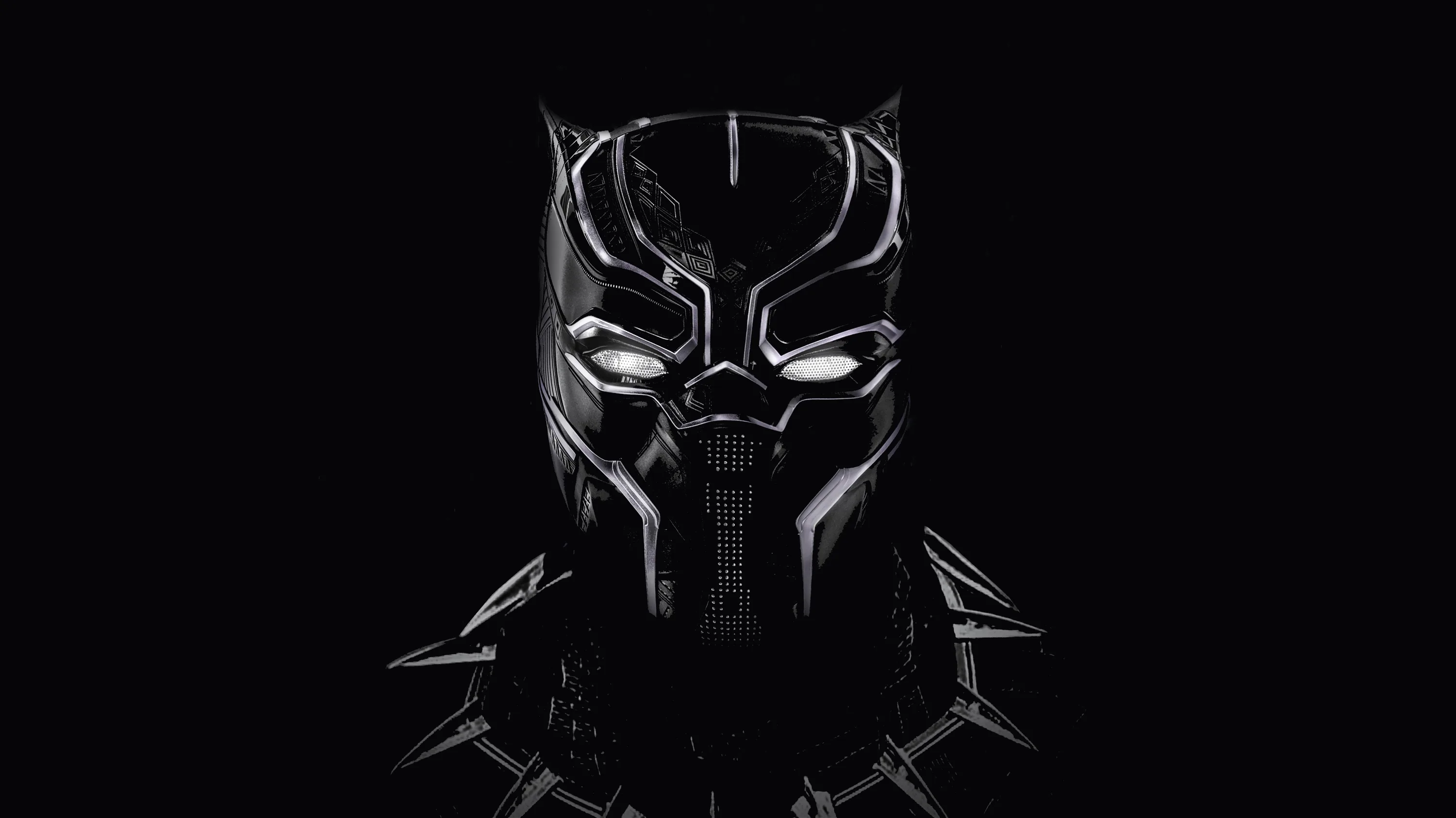 The Black Panther mask gleams out of darkness above a silver claw necklace, highlights tracing its ridges while both sides fall away to true black.