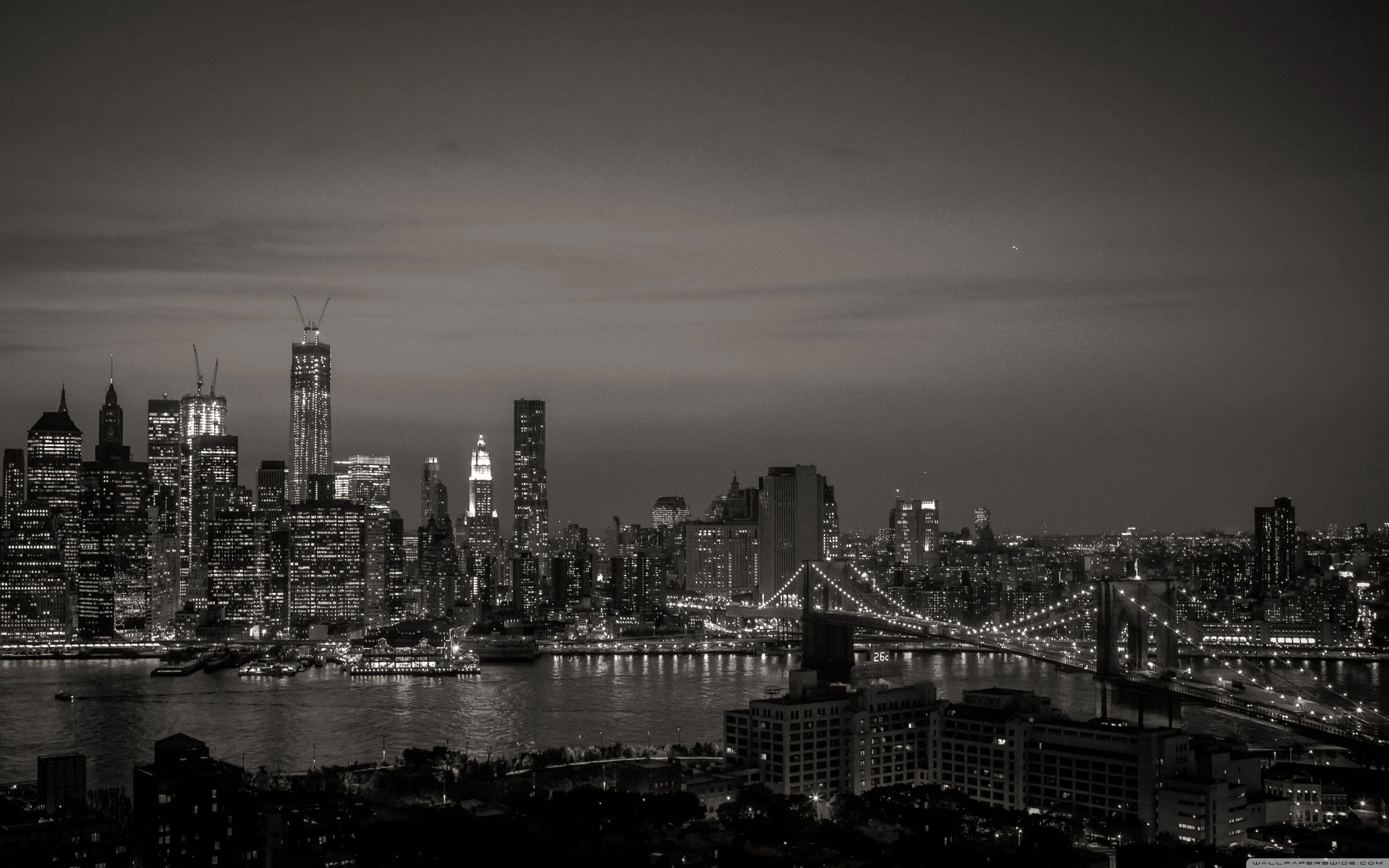 Manhattan's towers stand at the left while two lit bridges cross the river at the right, the whole top half plain grey sky.