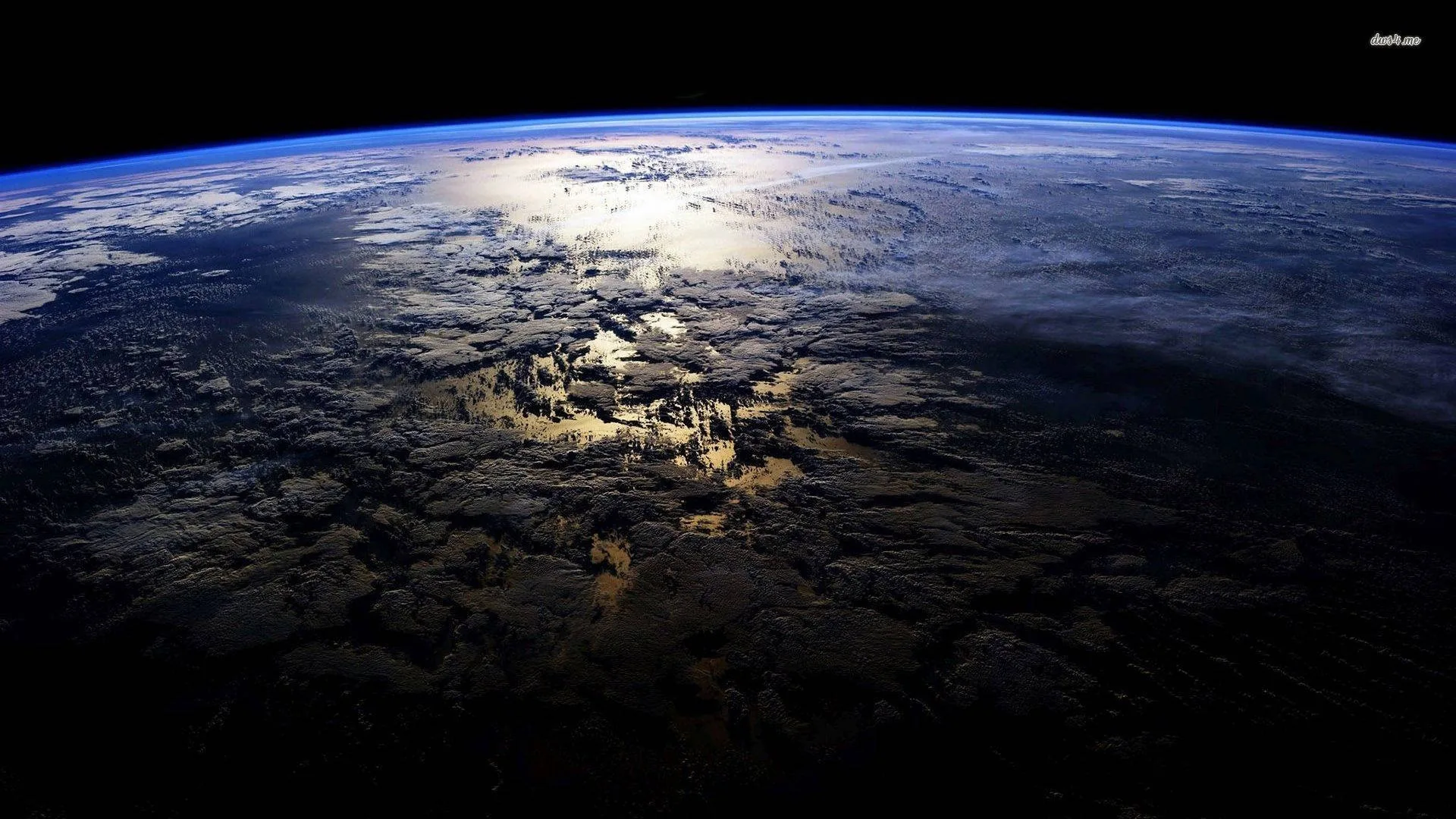 Shot from orbit, sunlight pools silver on the cloud tops mid-frame while the land below stays in shadow, the horizon fading out along the top.
