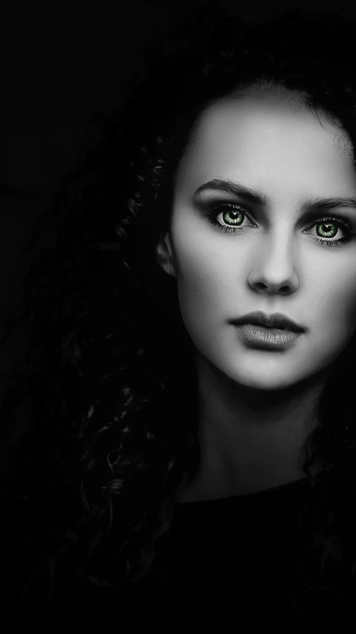 A close monochrome portrait against black, light falling across the eyes and one side of the face.