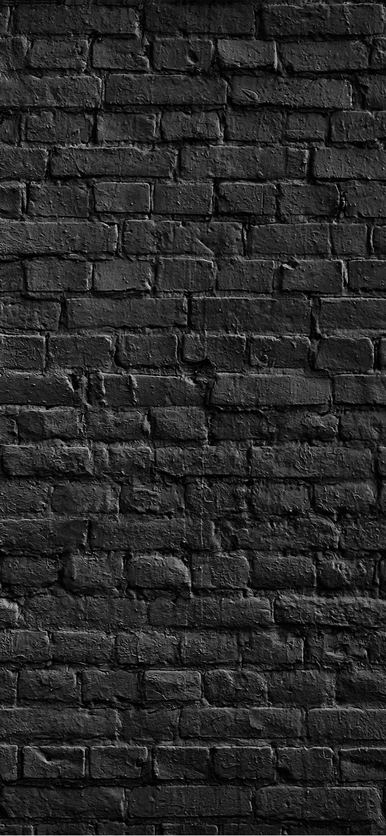 Weathered black brick fills a tall narrow frame, the mortar crumbling in places and the light dropping off toward both side edges.