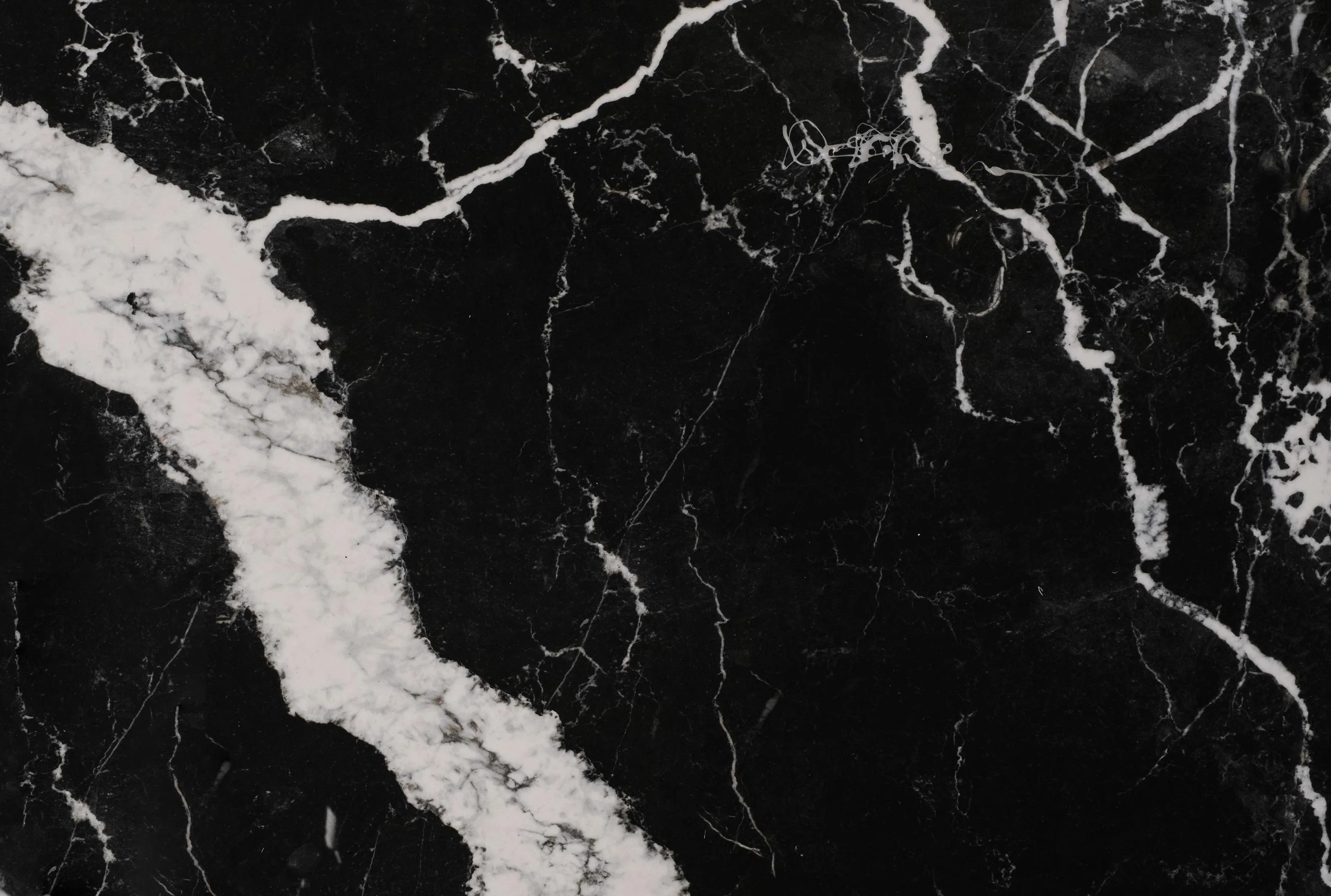 One broad ragged white vein climbs from the lower-left corner while hairline cracks fan across the right half of the polished black surface.