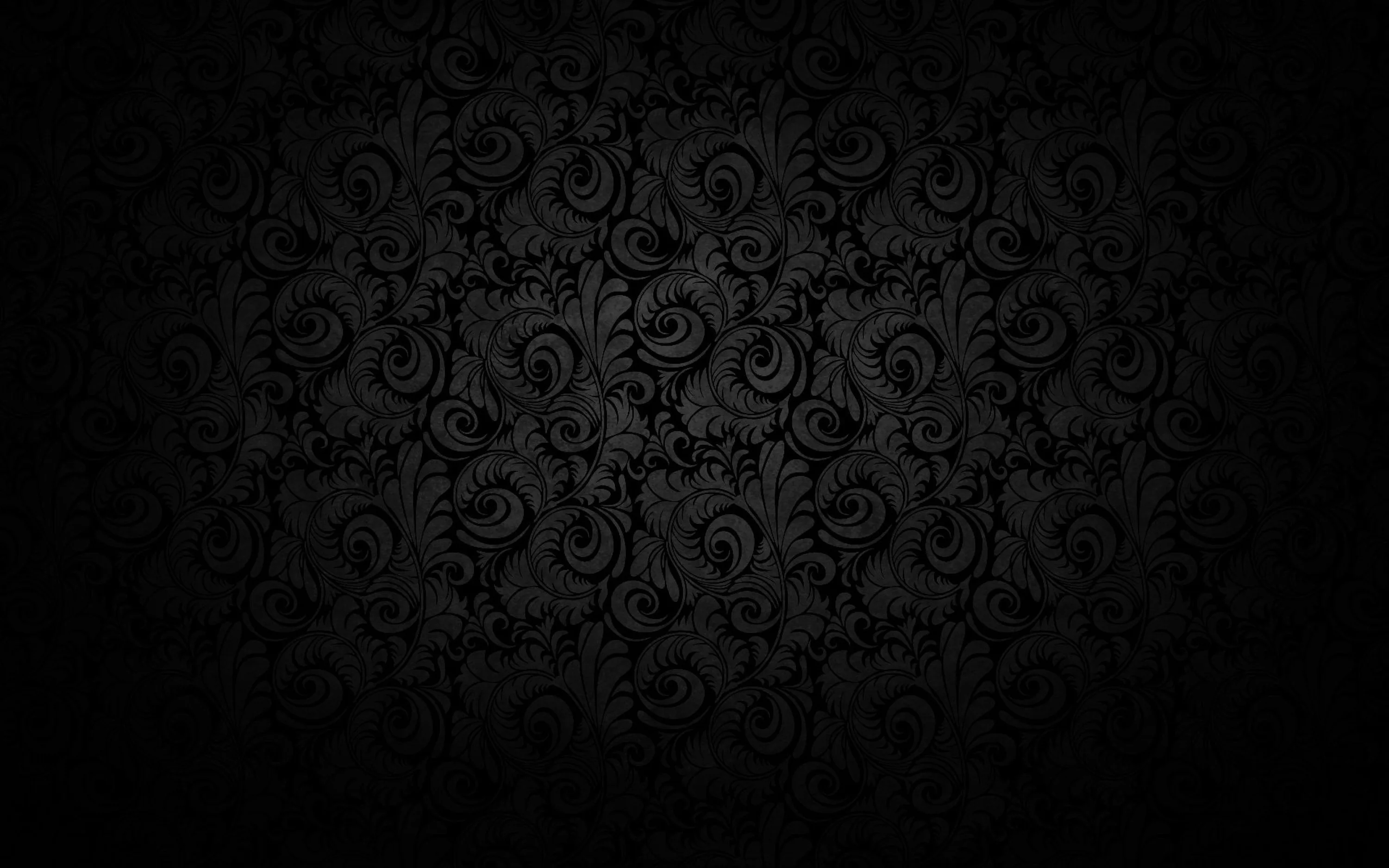 A repeating floral scroll printed in charcoal on black, lit softly through the middle and sinking into a heavy vignette at every corner.