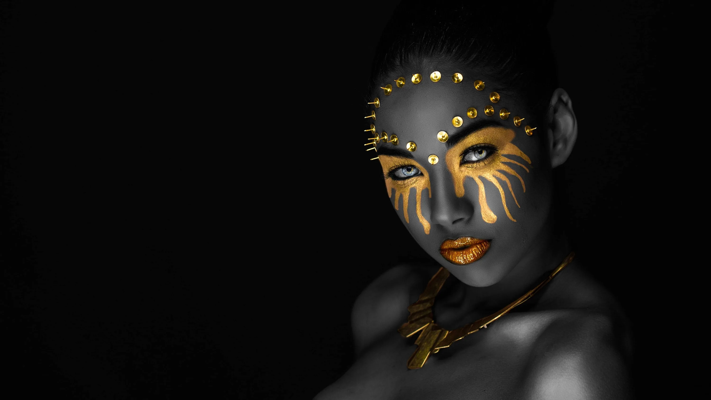 Flame-shaped gold stripes sweep across a woman's cheeks, dotted gold along her hairline, everything beyond her shoulders falling to flat black for OLED desktops.