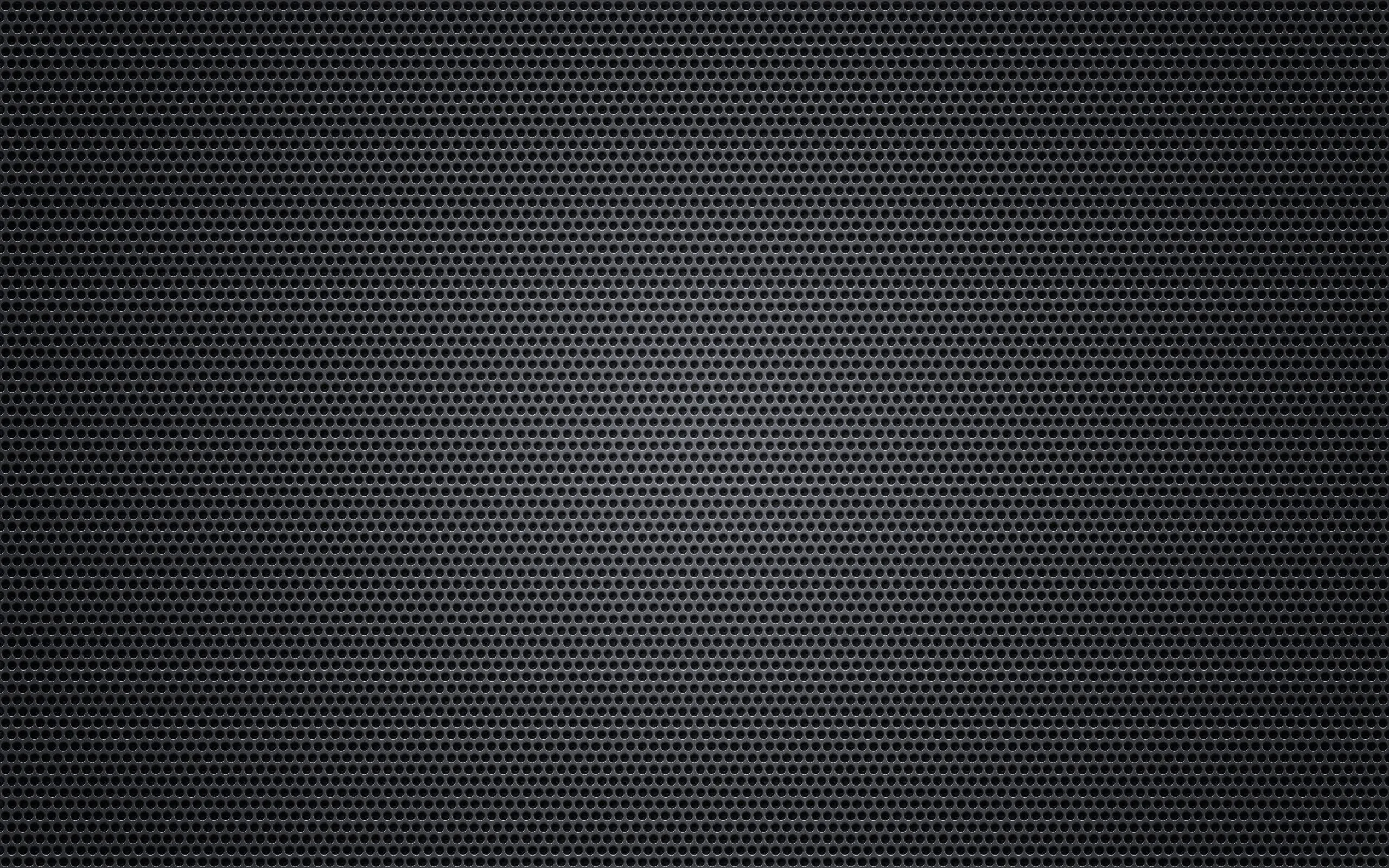 Thousands of tiny punched holes cover a dark grille, a faint glow lifting the centre while a soft vignette pulls every corner toward black.