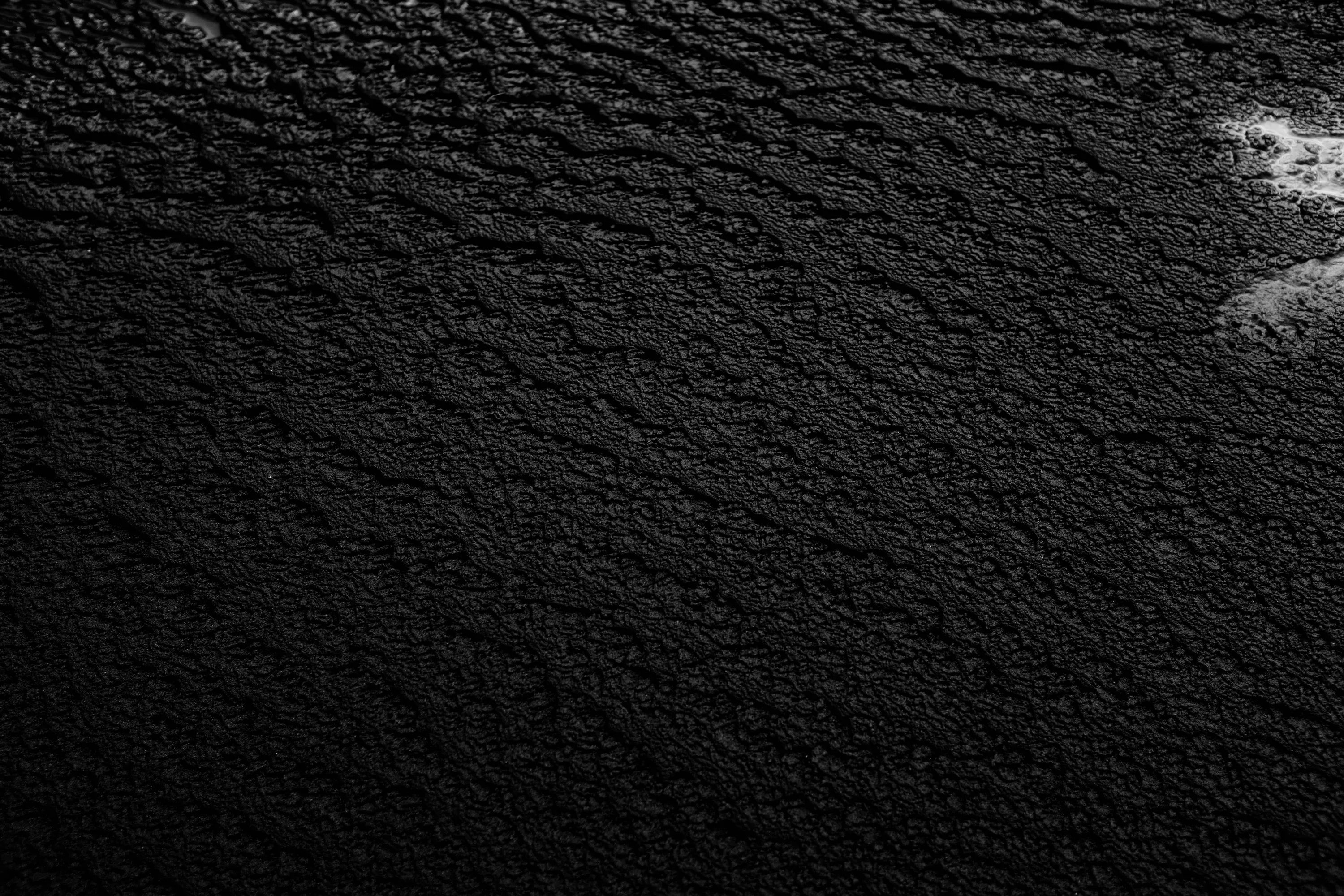 Small ripples run across a near-black grainy field, lit from the top right where a pale patch breaks the surface; the lower left stays darkest.