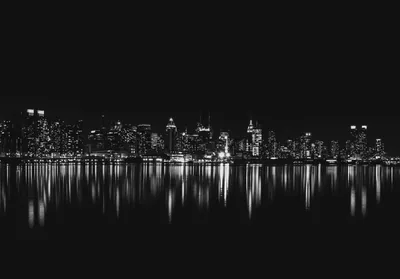 Manhattan towers glow in a thin band of monochrome light, the whole city mirrored in still black water below with empty sky above.