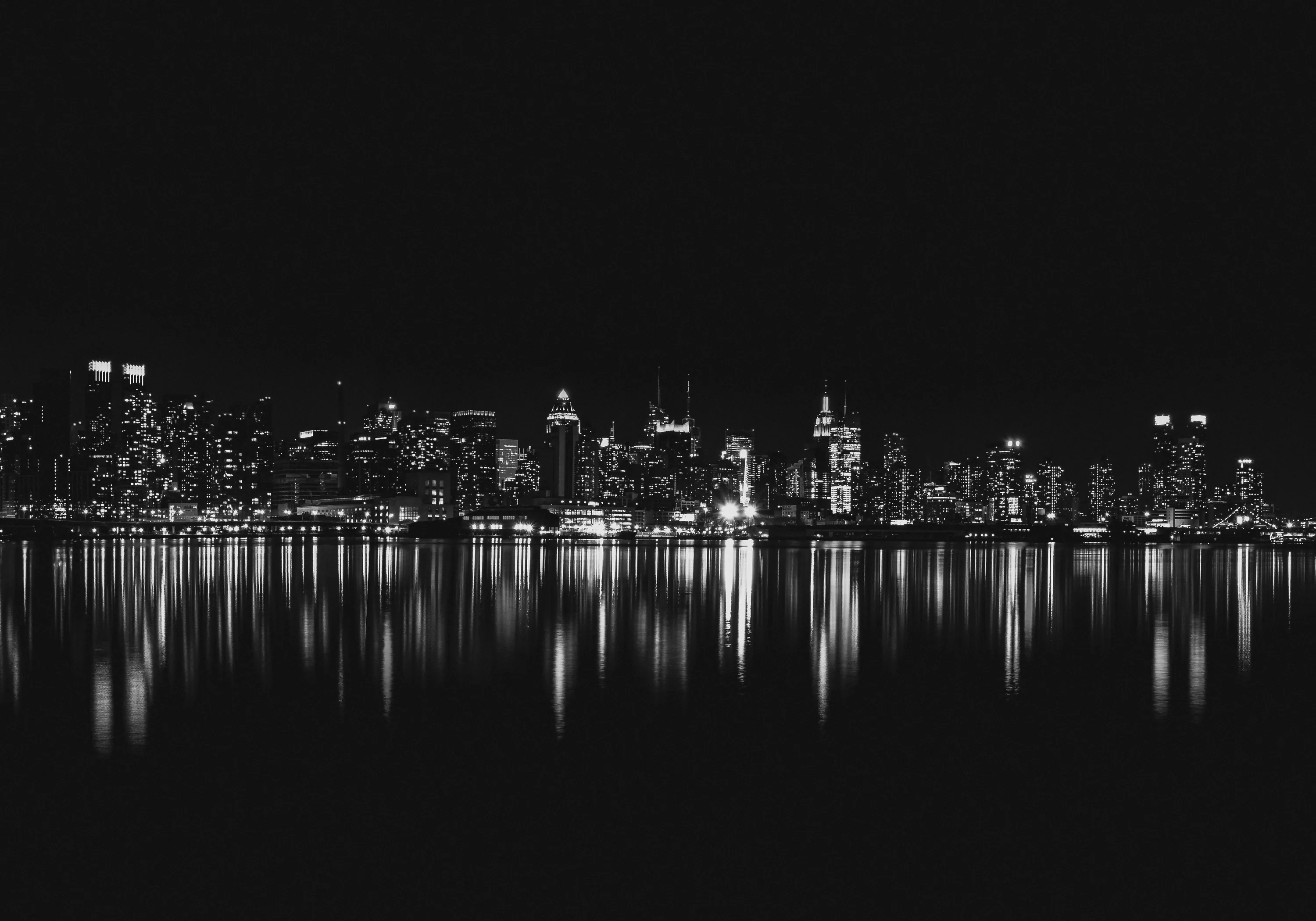 A dense skyline burns white against black sky, every tower repeating in the flat water across the foreground.