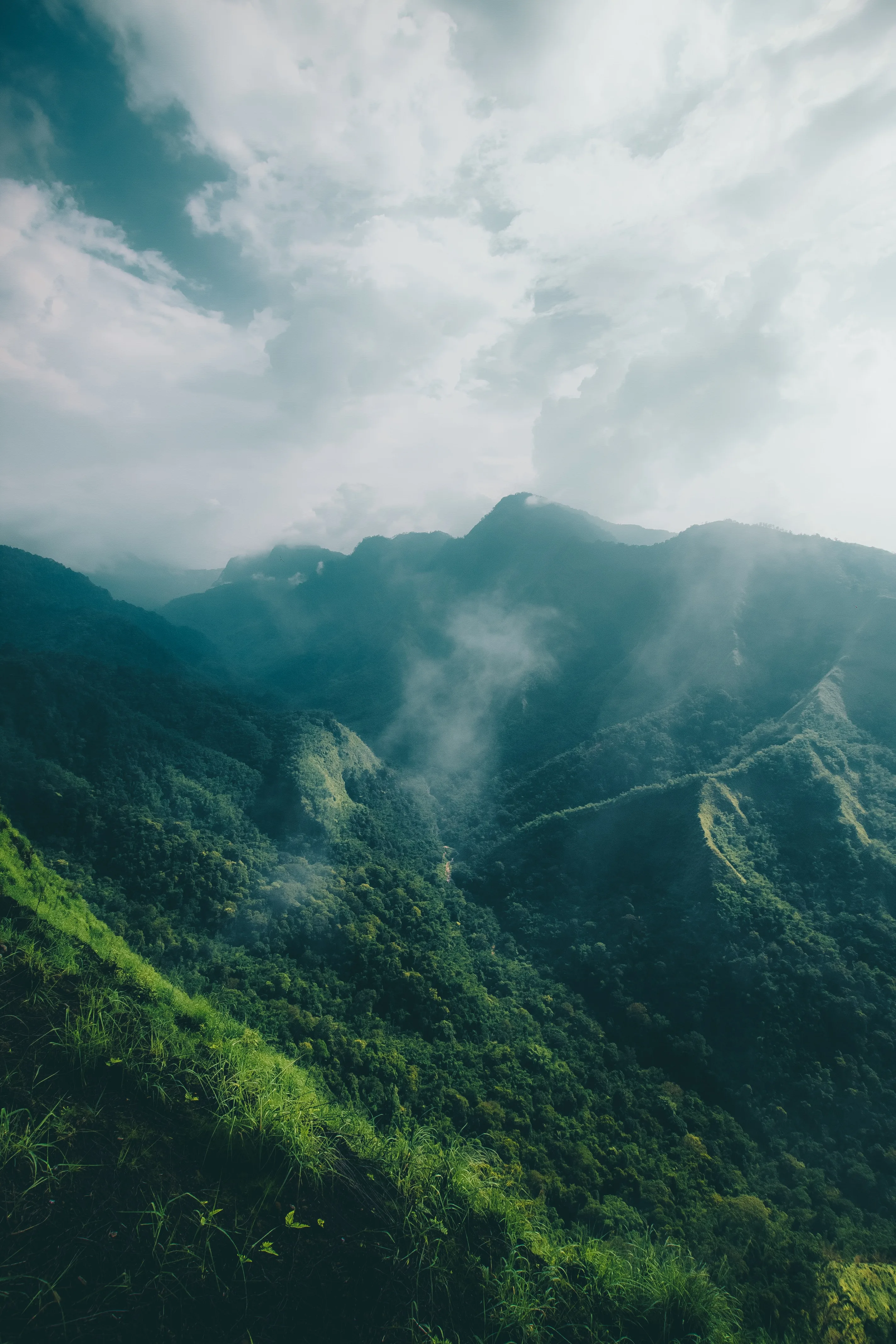 Steep jungle-covered ridges climb into drifting mist under a bright white sky, the hazy upper third leaving clear space for a phone clock.