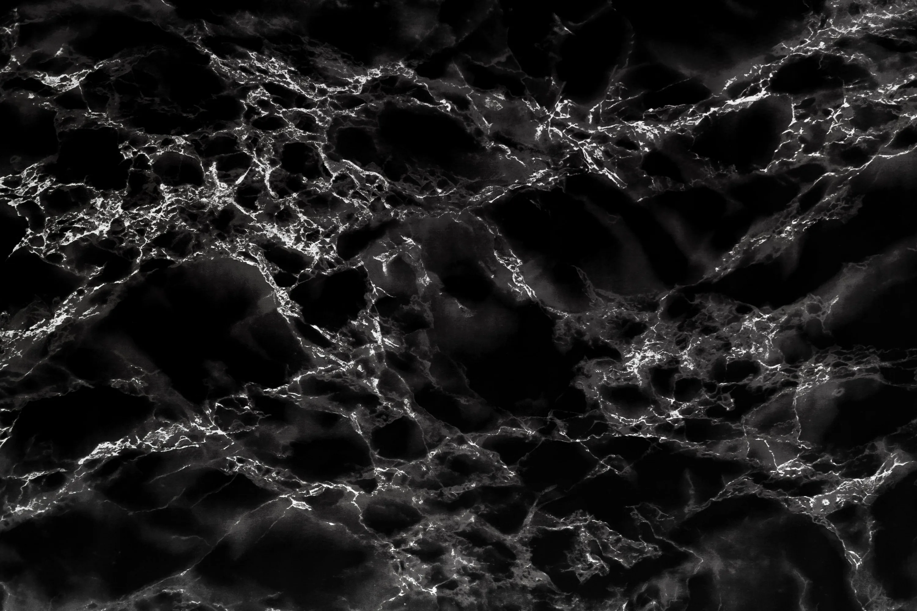Mottled grey veining drifts in loose horizontal cloud bands across the slab, dark hollows opening at upper-right and lower-left, the whole surface soft rather than sharp.