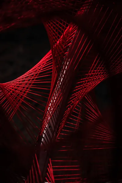 Taut red threads stretch between unseen anchors to form twisting hourglass shapes, the background dropping away to black behind them.
