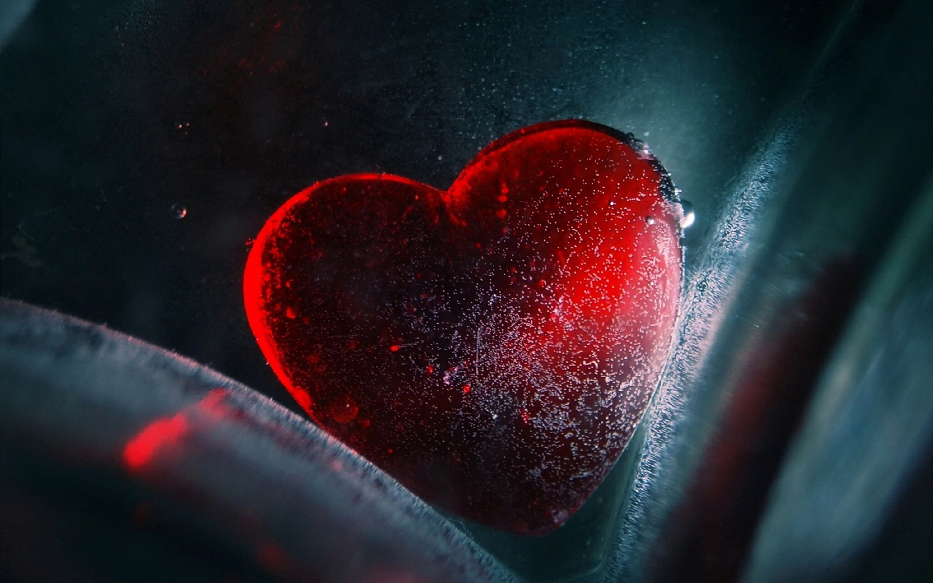 A macro shot of an ice-crusted heart pressed behind curved glass, a faint red glow spilling into the lower left while the right edge stays cold grey.