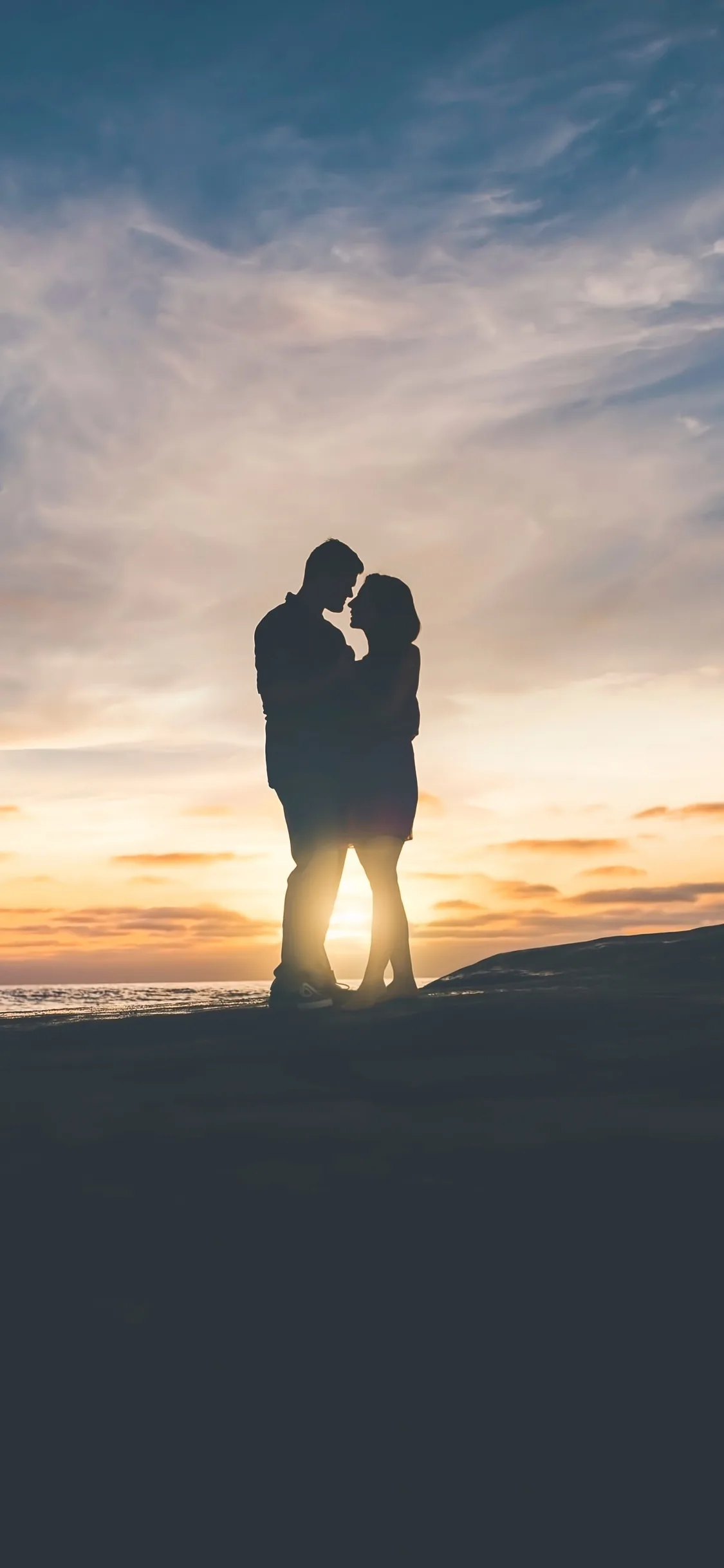 The low sun glows right behind their joined silhouettes at the horizon line, pastel blue above fading warm below, and the bottom quarter drops to solid black.