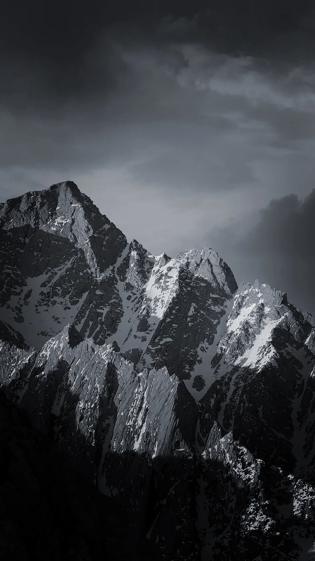 A snow-streaked peak fills the lower half in hard grey, heavy cloud dragging across the summit and the rock face falling into shadow on the right.