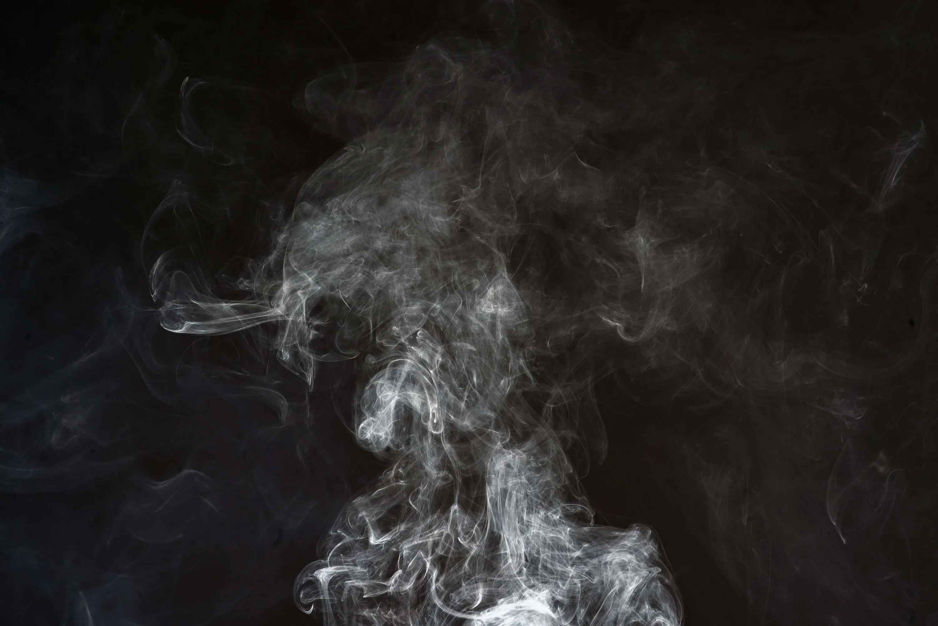 A soft grey plume drifts up through the middle of the frame, edges dissolving into haze, with the darkest black held in both upper corners.