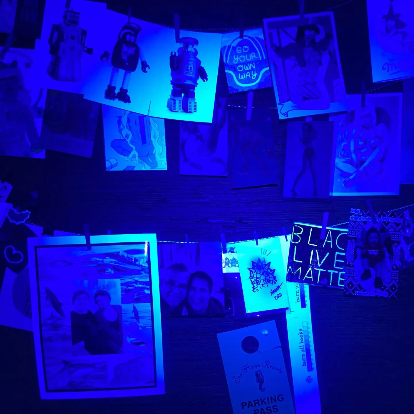 Snapshots and posters pegged to strings glow deep blue under UV light, covering the wall edge to edge with no quiet space for widgets.