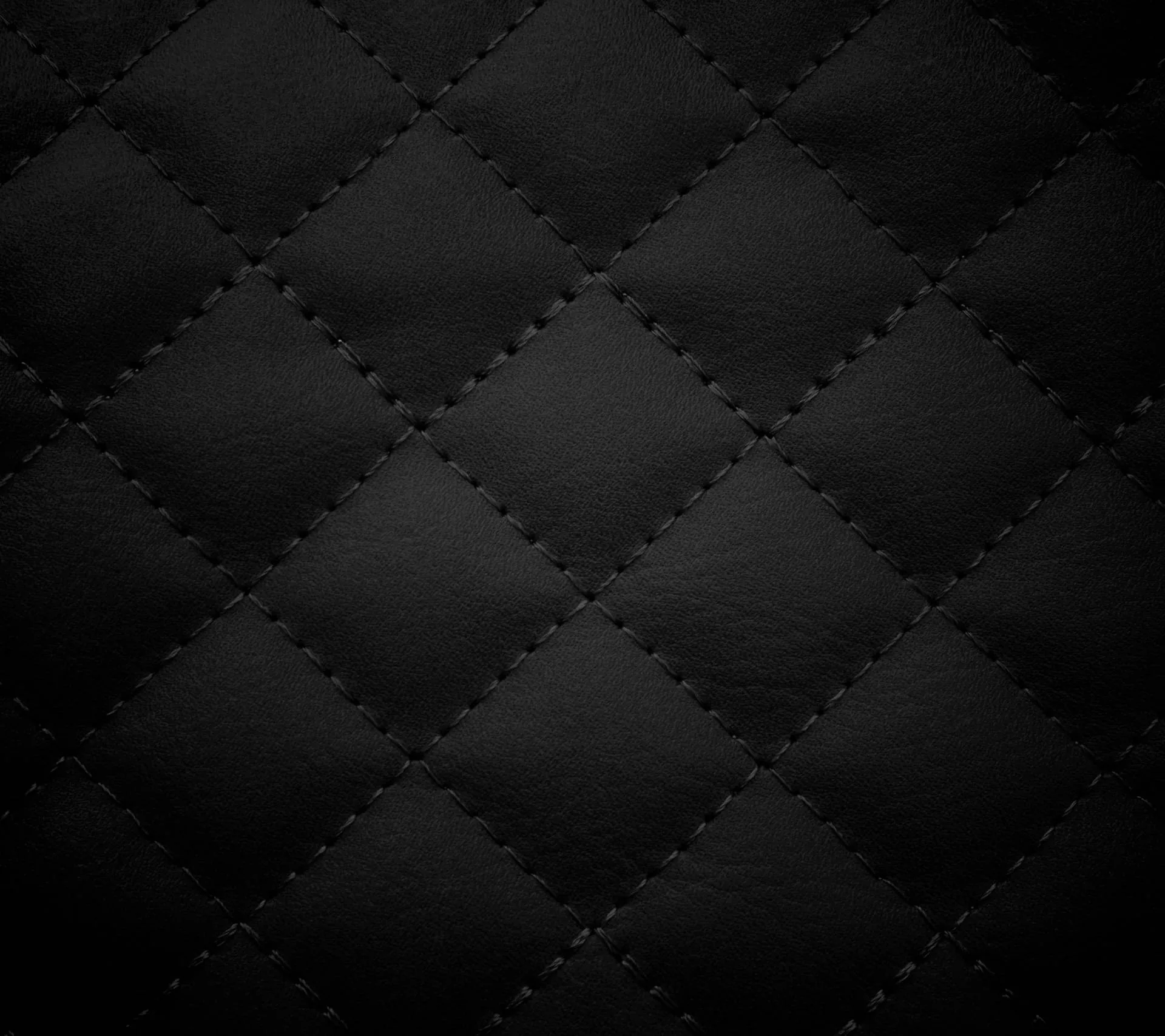 Padded black leather diamonds meet at dotted stitch lines, the padding catching just enough light that each cell shows a soft rounded bulge.