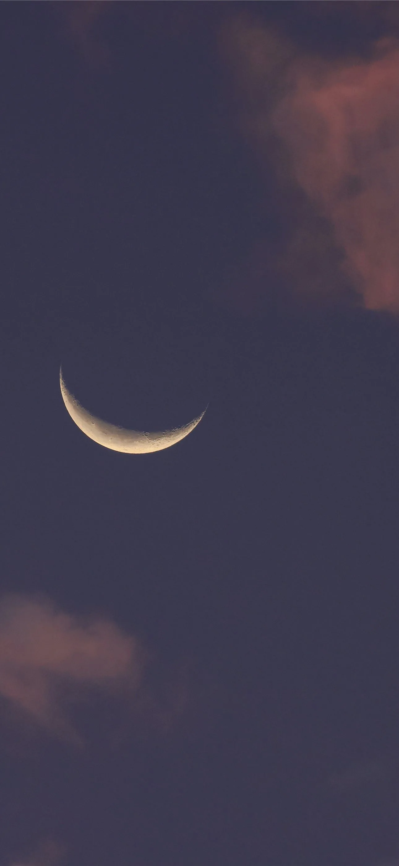 A thin crescent hangs left of centre in a mauve dusk, soft clouds catching the last light in the top and bottom corners.